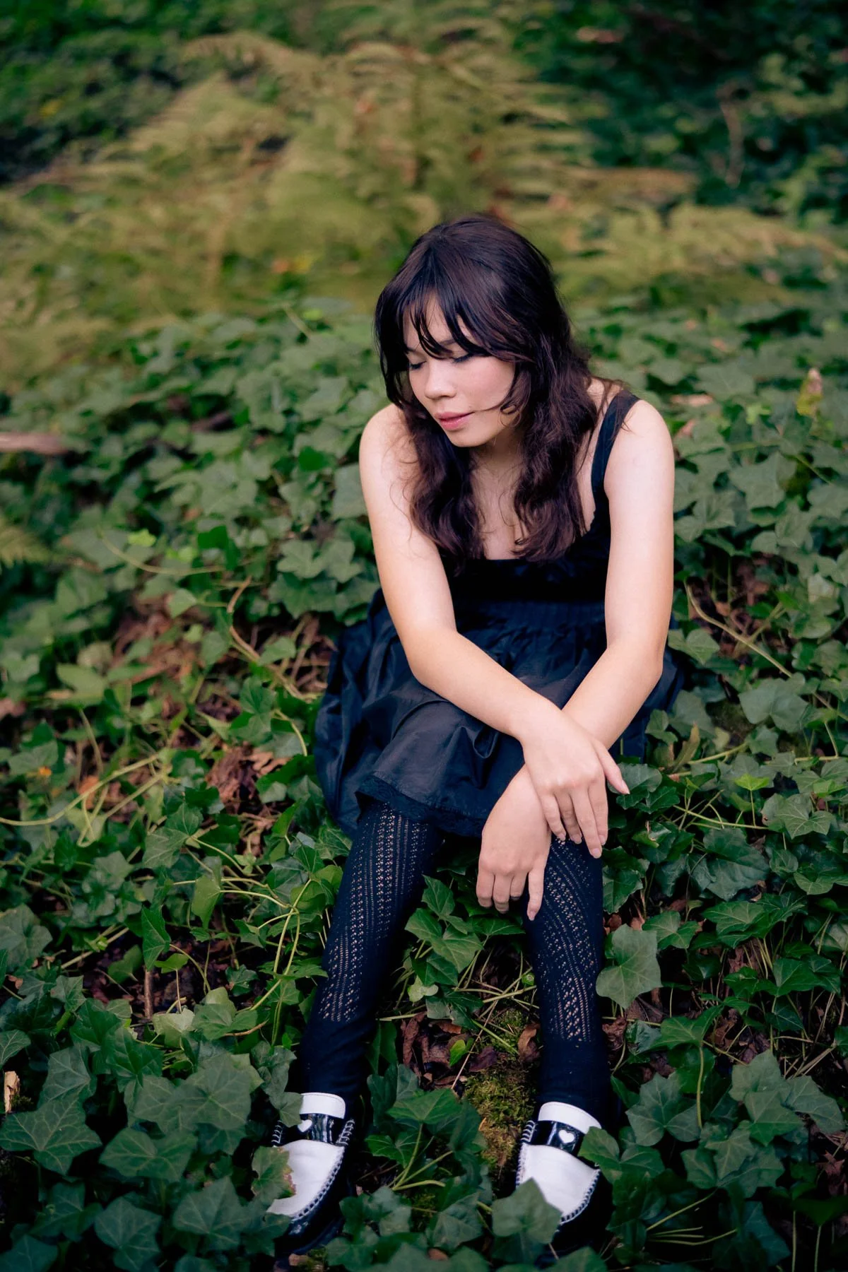 Sitting on forest floor, a girl in all black poses for a senior portrait
