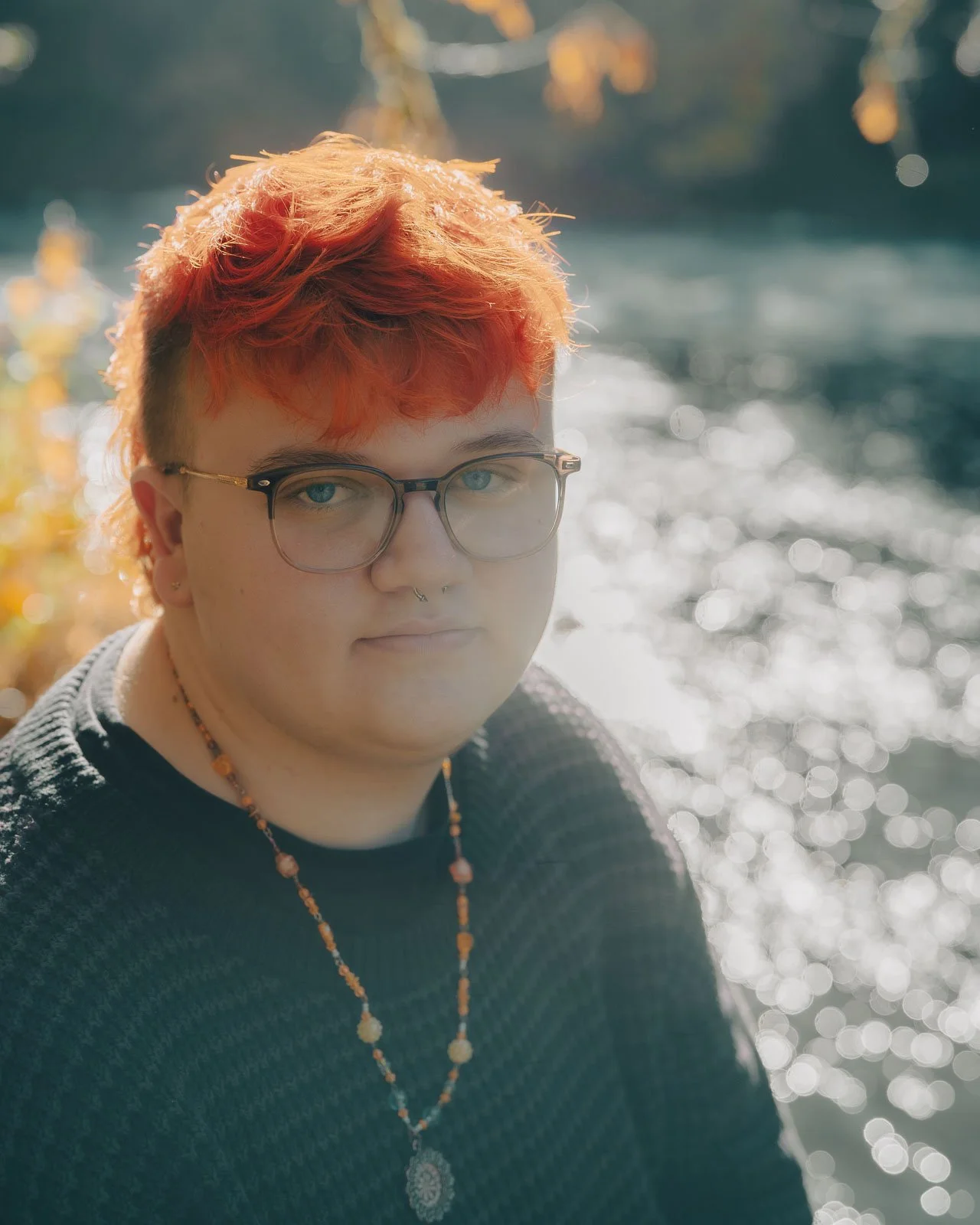 A high school senior with orange hair sitting in front of a river