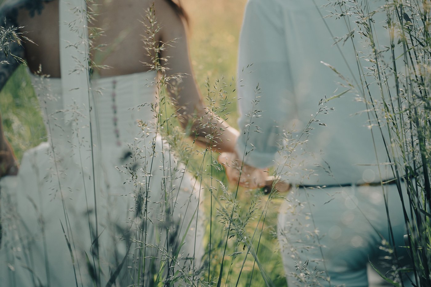 A couple dressed in white holding hands and walking through tall golden grass