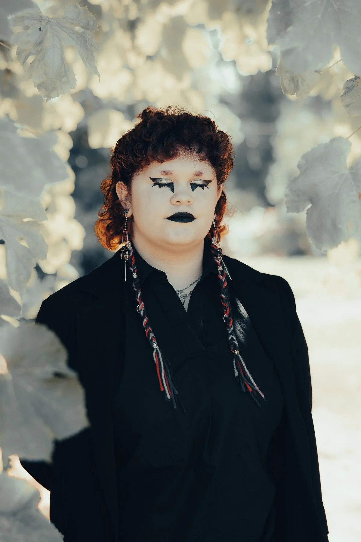 A girl in goth makeup with her eyes closed, surrounded by white blooming flowers