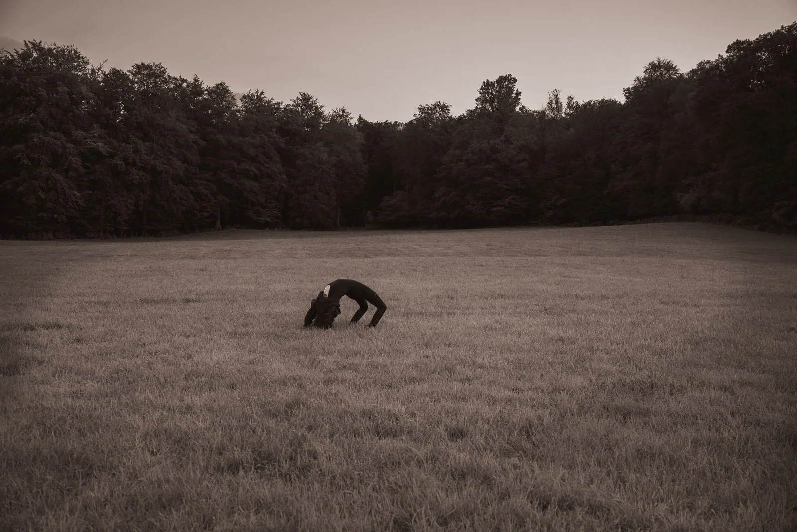 A girl doing a backbend in a large open meadow surrounded by trees