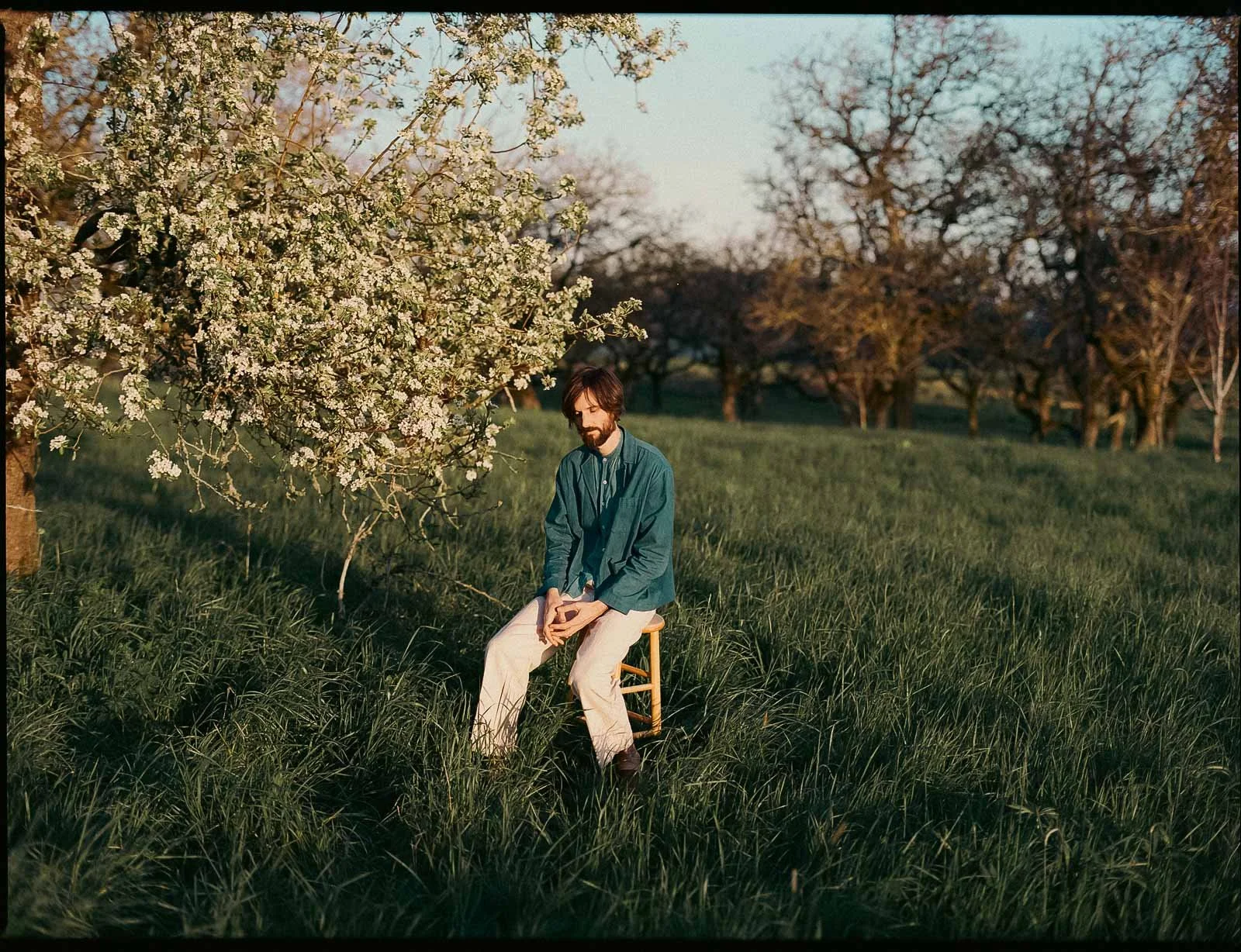A musician poses for an album portrait at Powell Butte, in a large meadow next to a flowering tree
