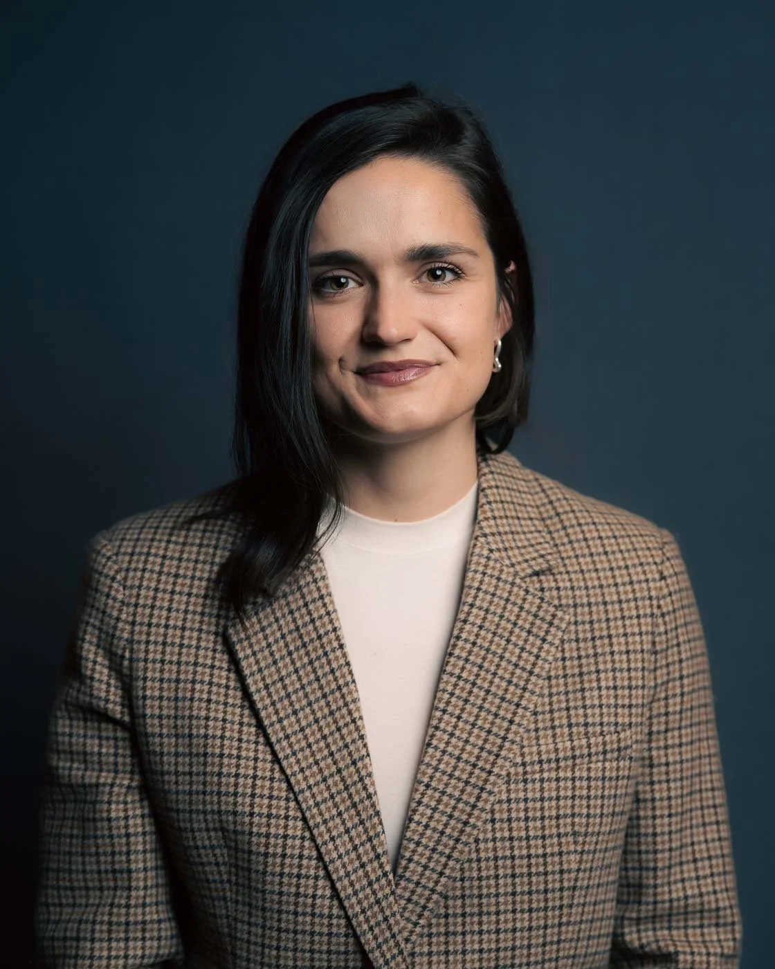 Studio headshot of a woman in a tweed jacket set against a dark blue background