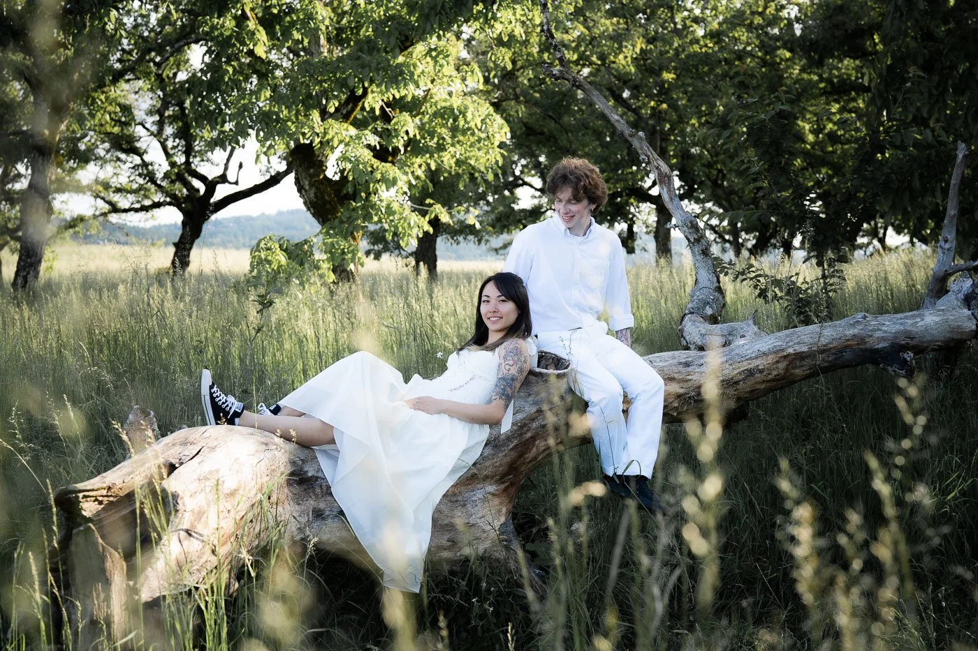 A couple lays on a downed tree in a field of tall grass
