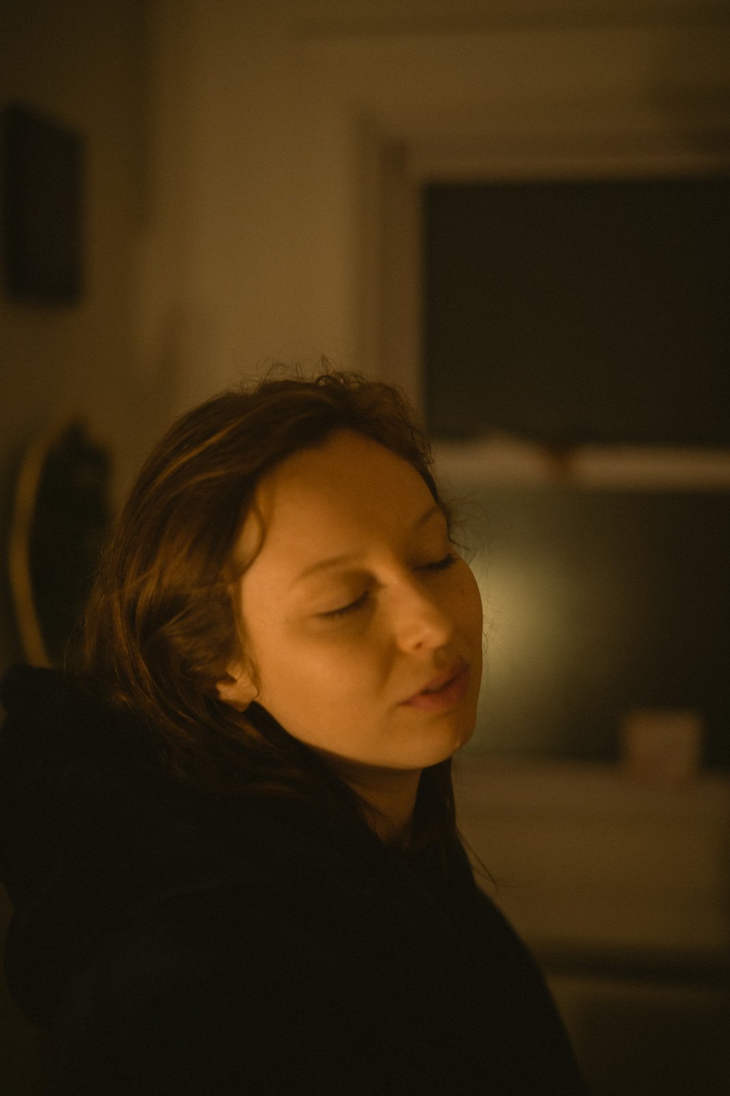 A girl stands peacefully in a small room with her eye closed