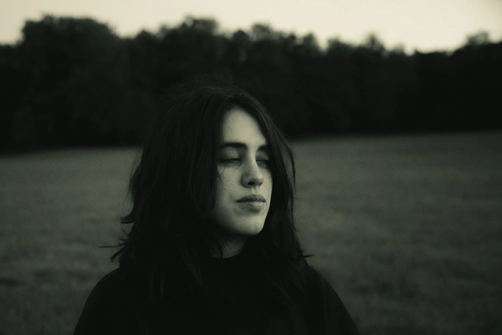 A girl with her eyes closed standing in a large open meadow