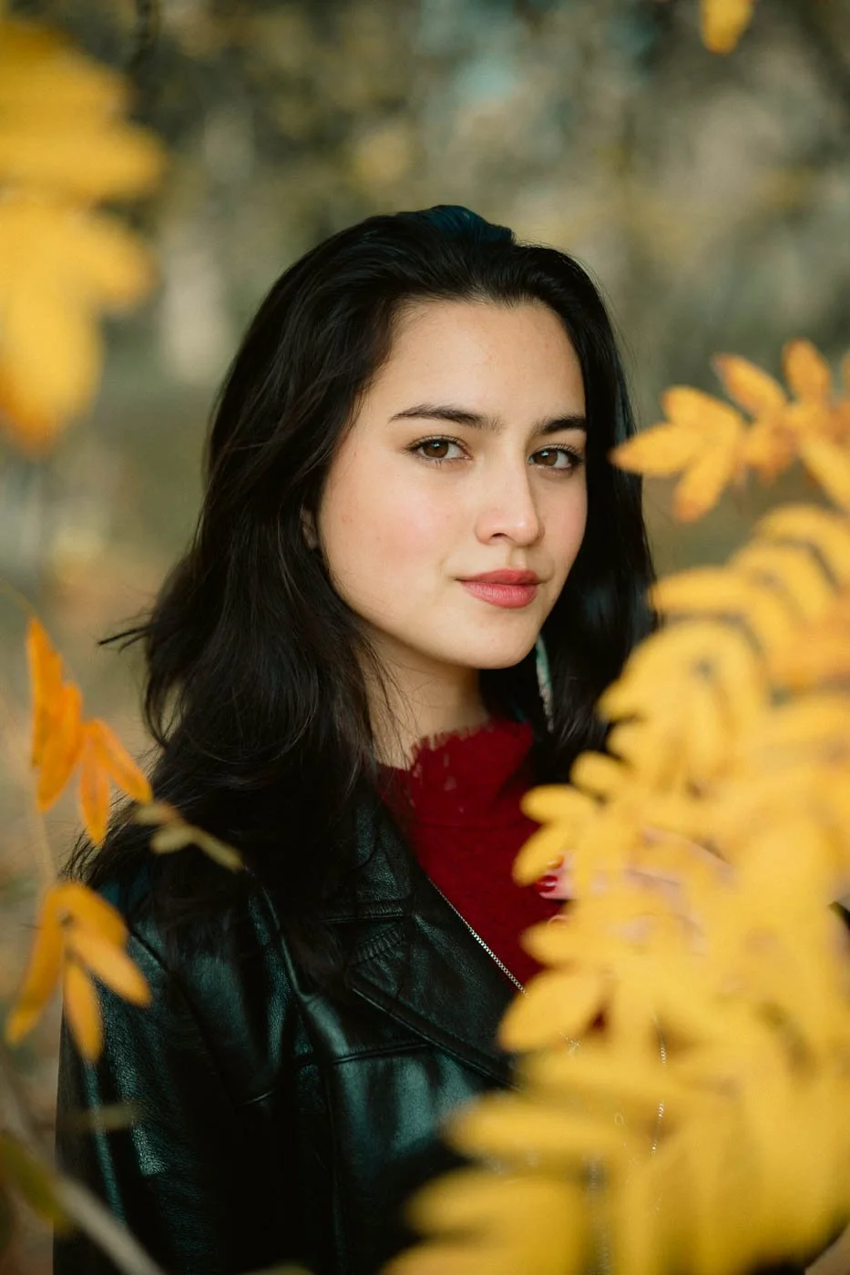 Stylish girl in a leather jacket surrounded by leaves in Fall colors