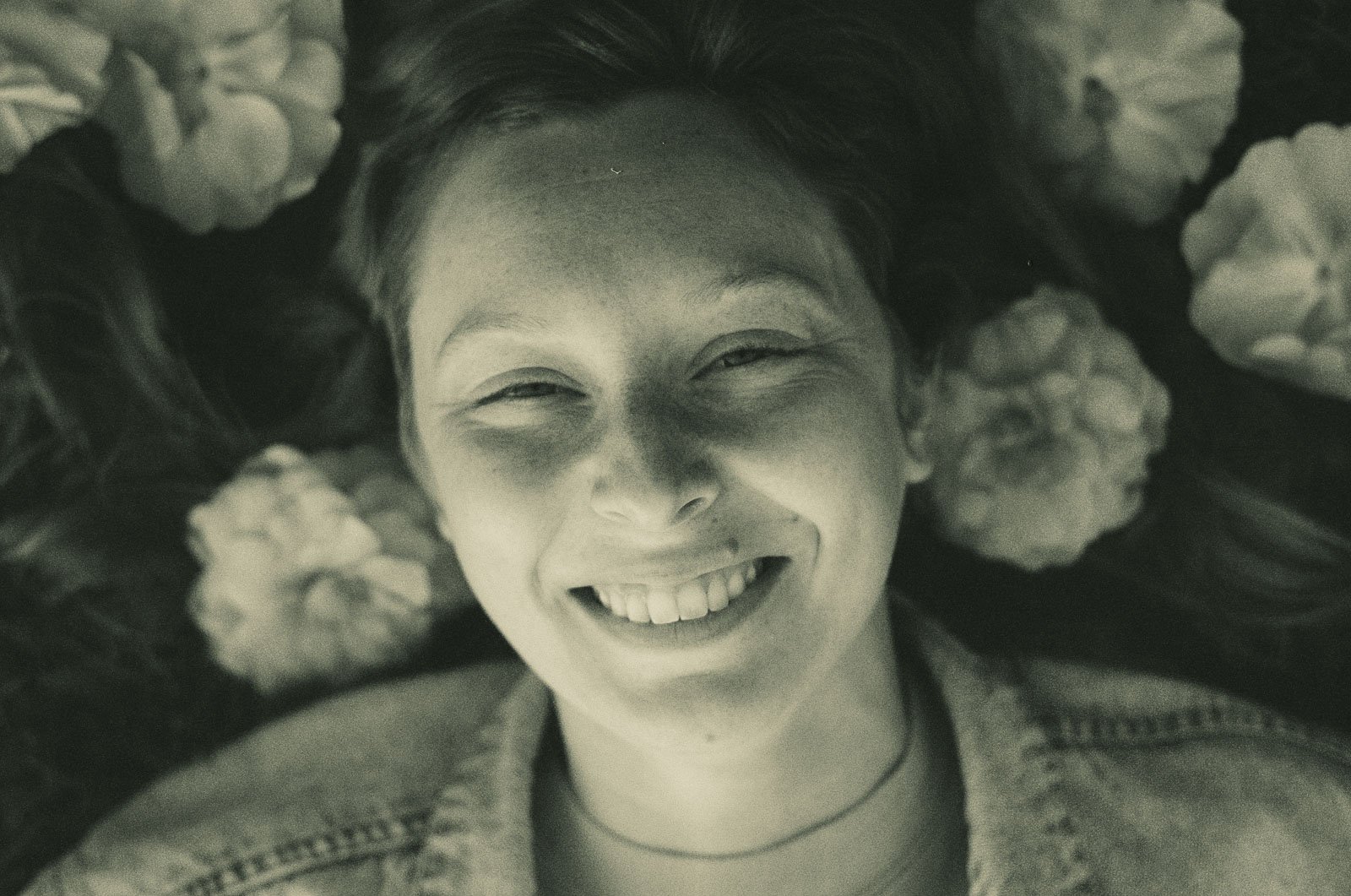 A smiling girl laying on the ground surrounded by flower petals