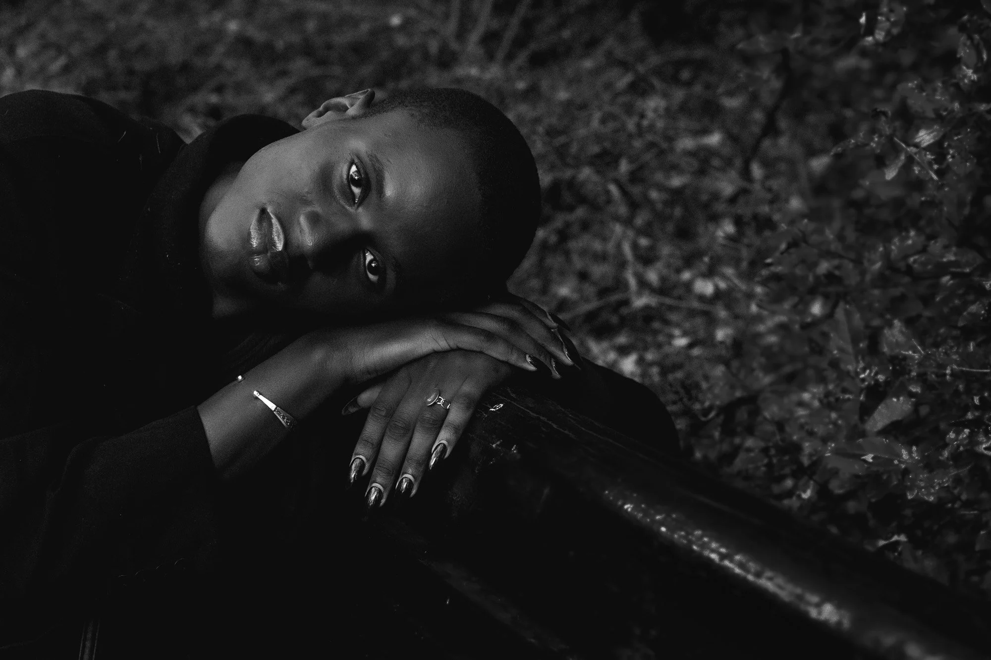Modeling portrait of an elegant black woman leaning her head onto the back of a bench in a park