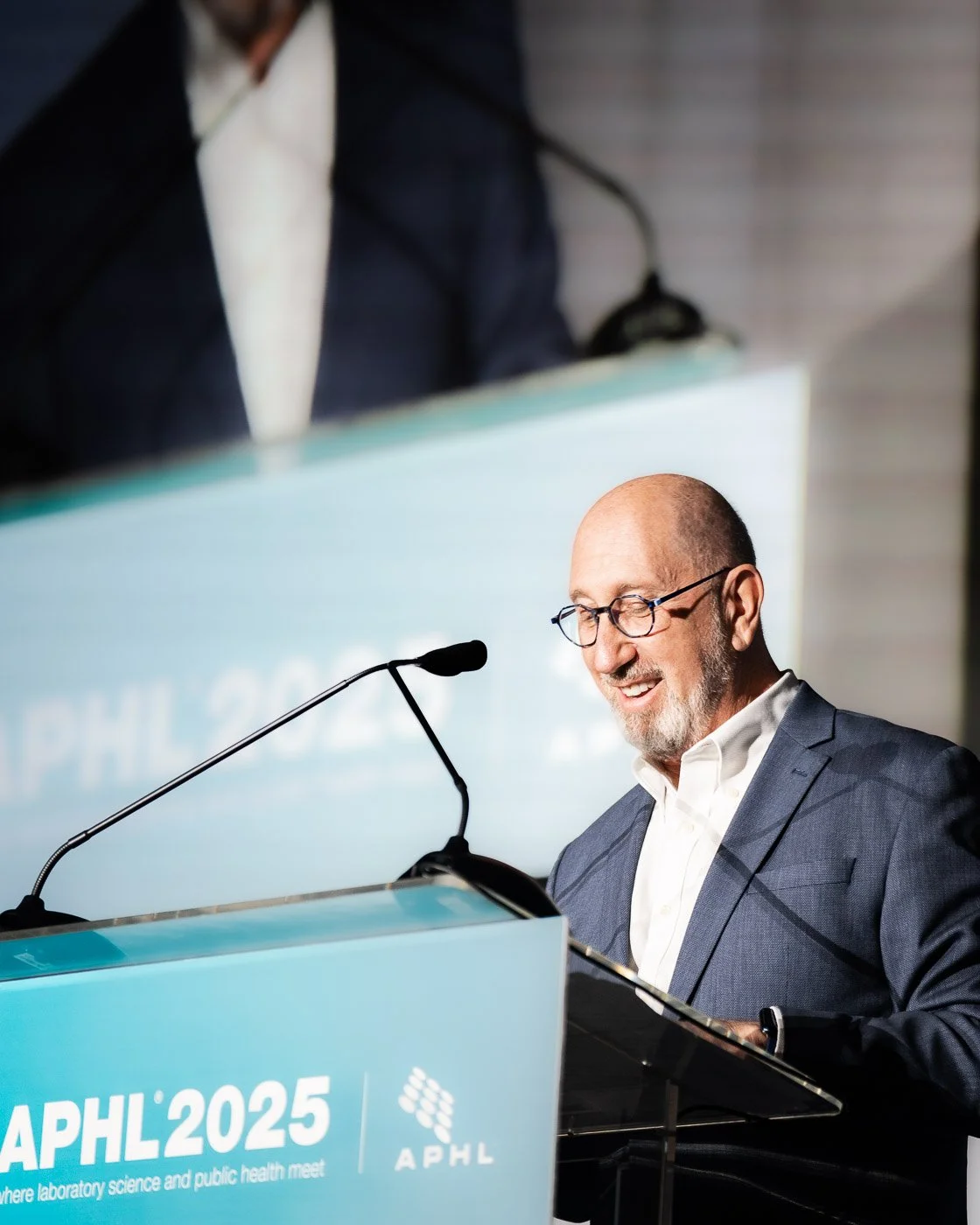 Smiling man presenting on stage at an APHL conference