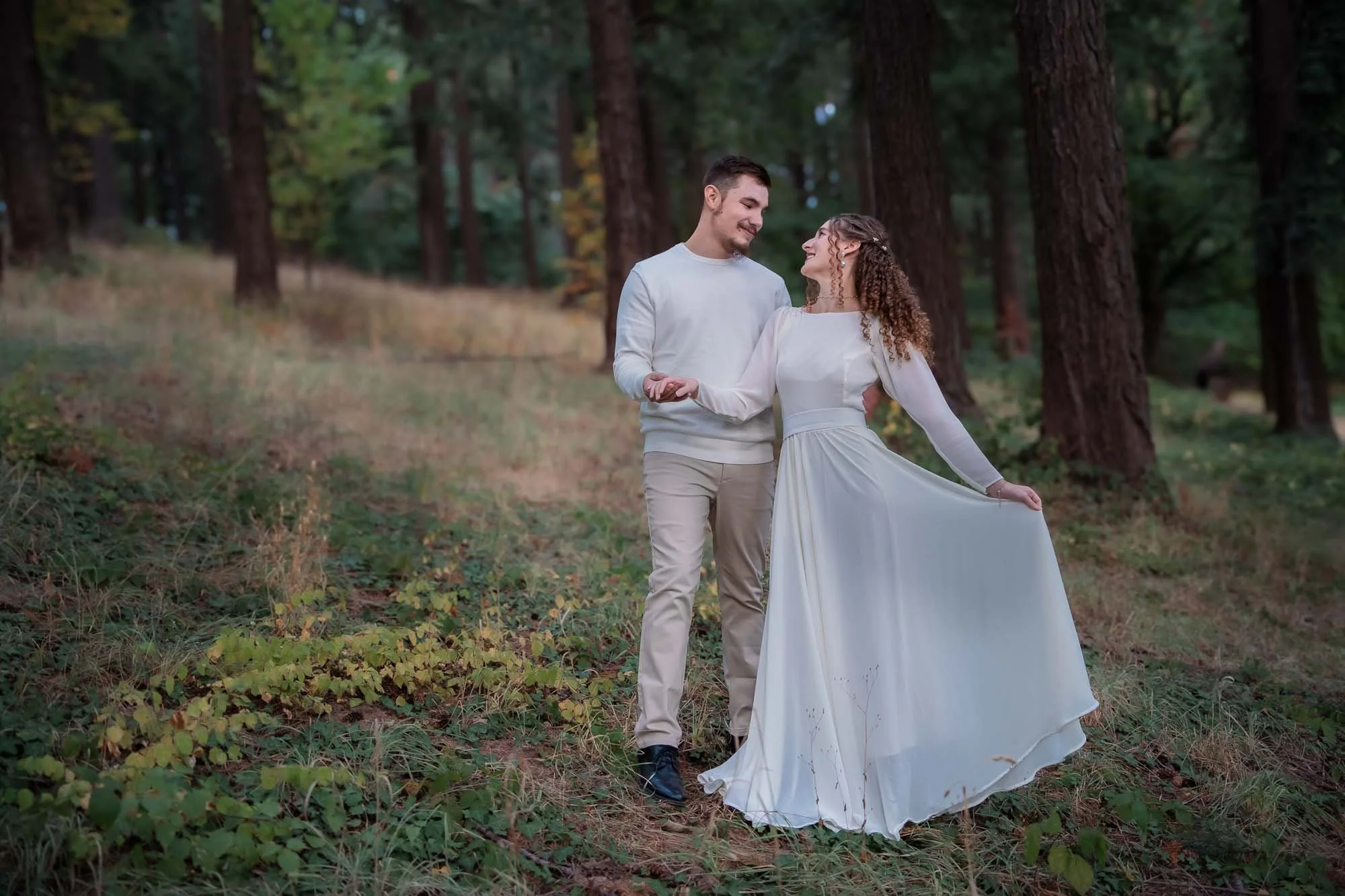 A smiling couple in matching white dance in the forest of Mt Tabor
