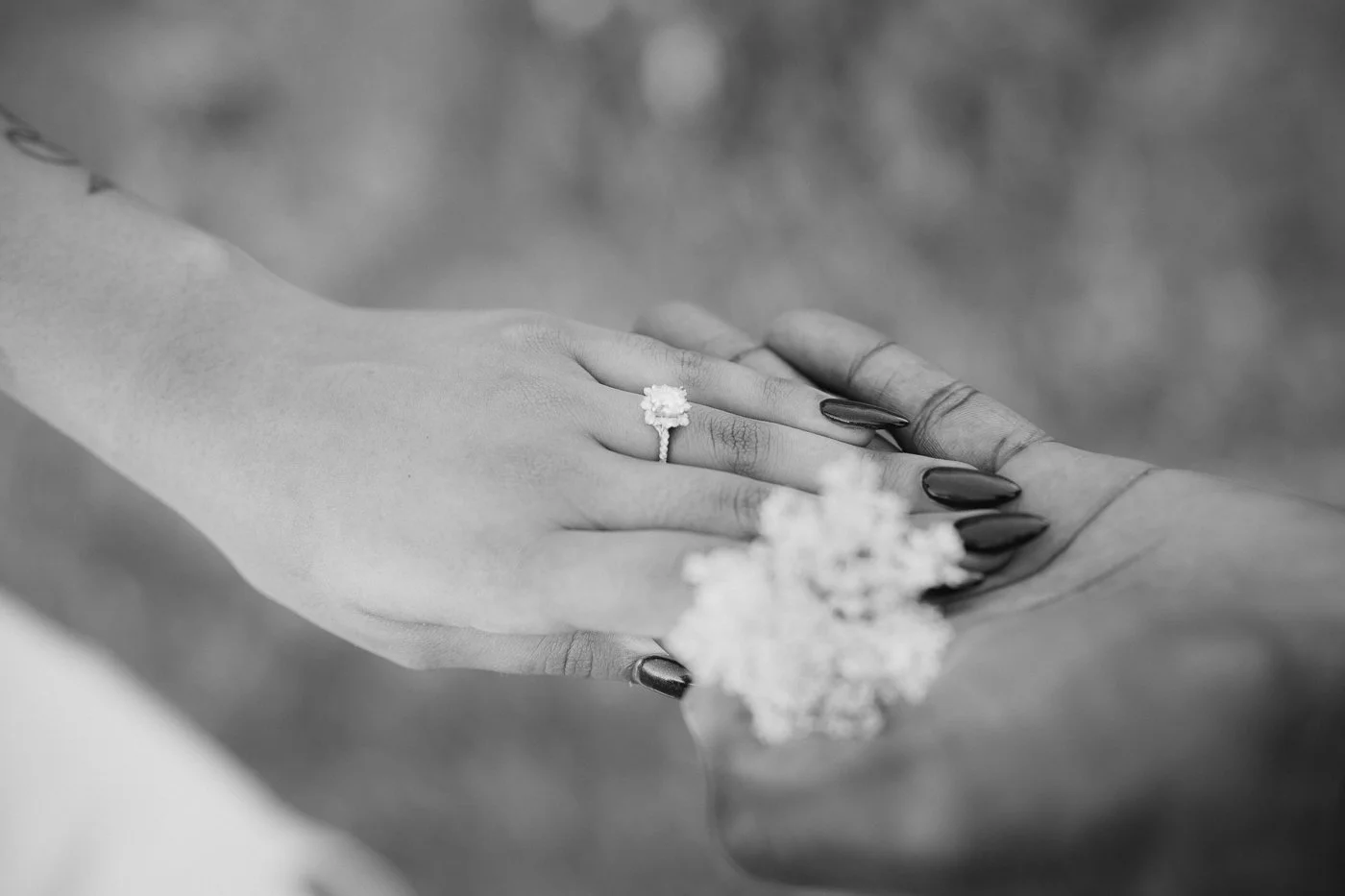 An engaged couples hold hands with their engagement ring and flowers