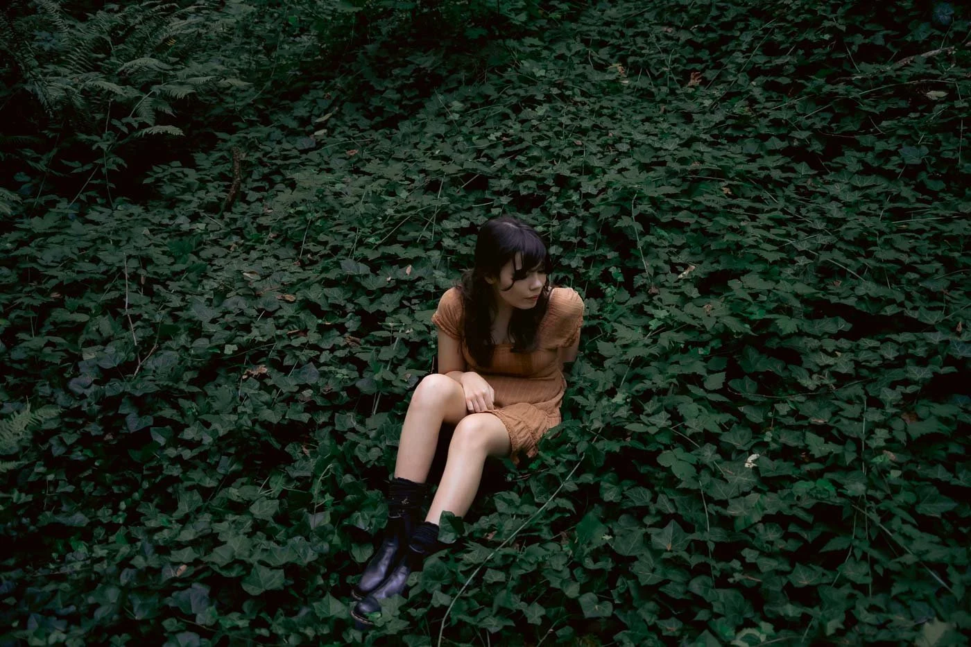 A high school senior girl sits on the forest floor surrounded by English Ivy