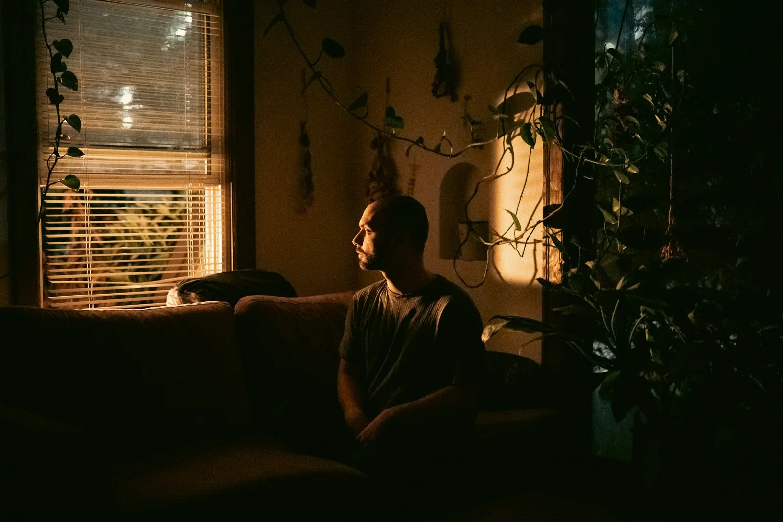 A man sits in a living room looking out the window with a bright light coming through