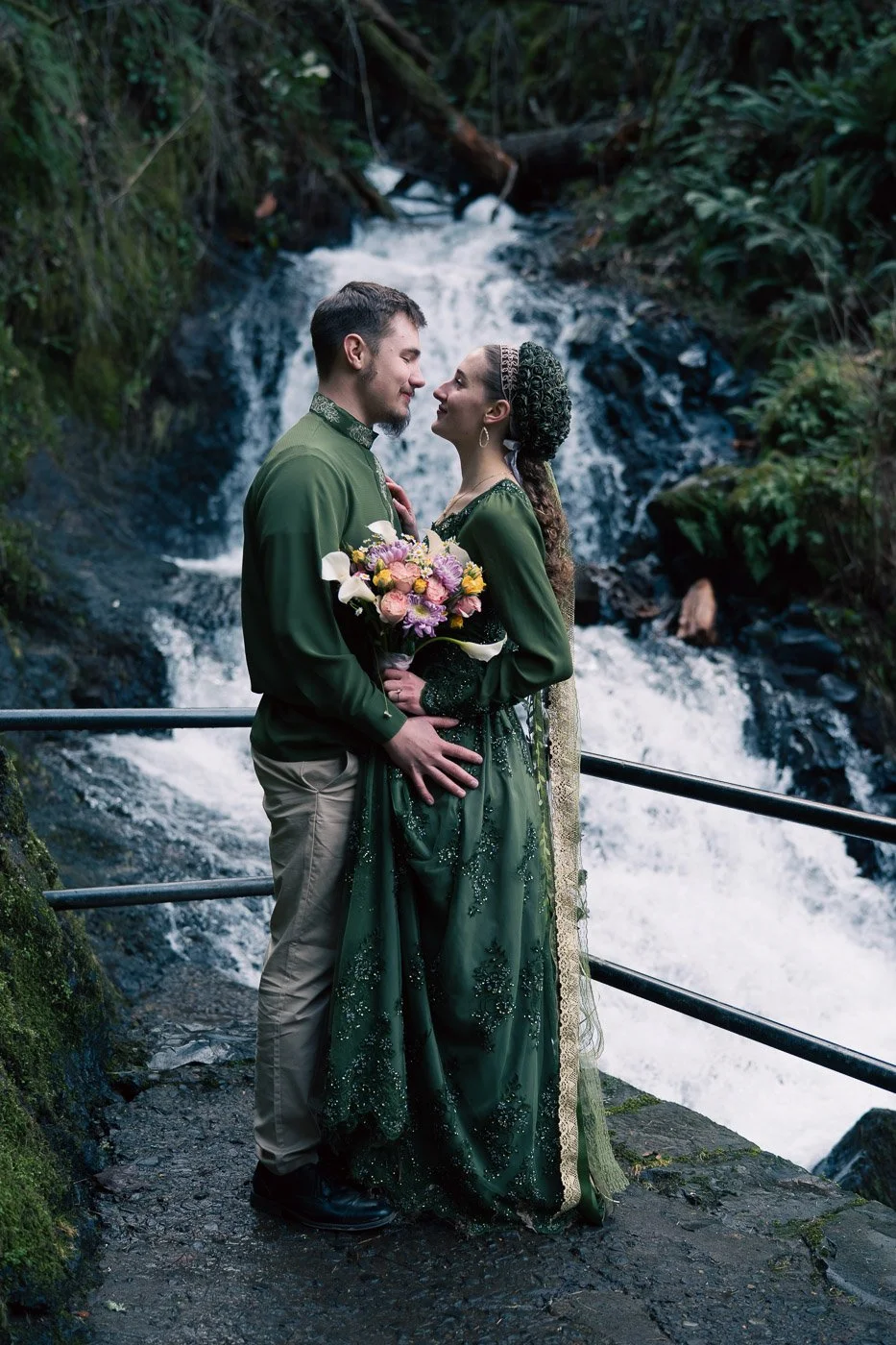 A bride and groom in matching green, eloping next to a waterfall