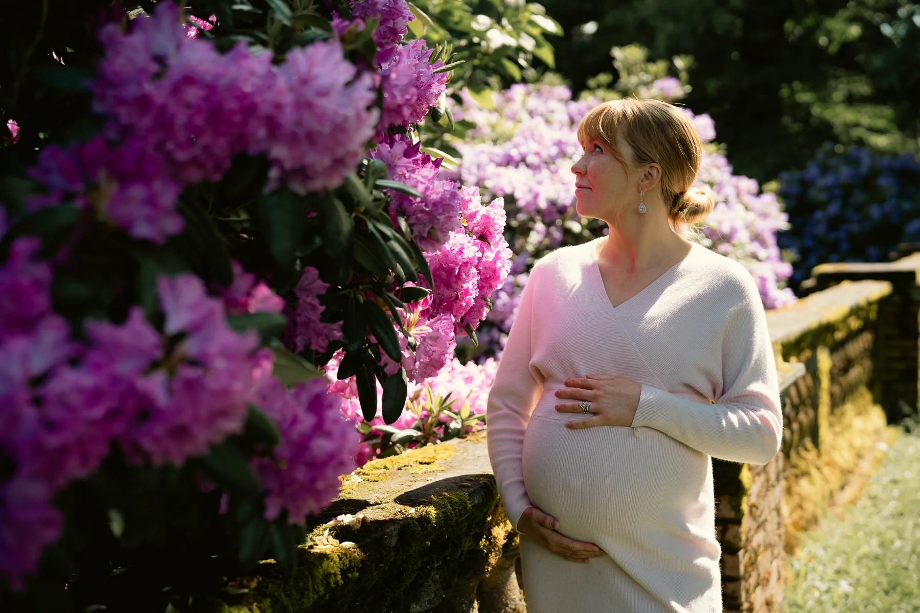 Smiling pregnant woman in a light pink dress looking at flowers in a nature park