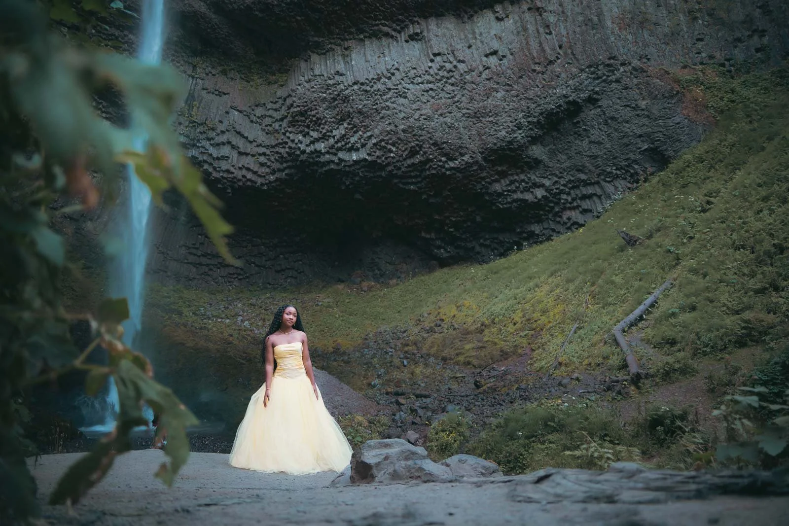 A young girl in a yellow dress poses for a senior portrait underneath Latourell falls