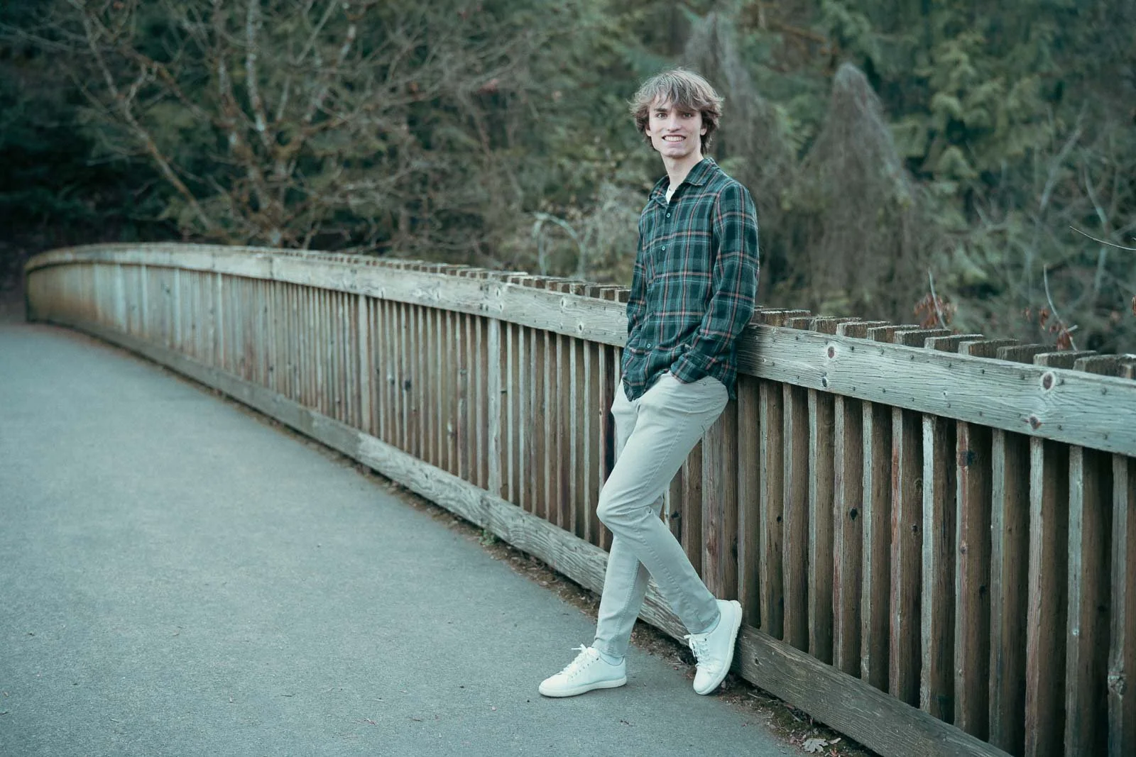 Smiling high school boy leaning on a bridge railing in a nature park