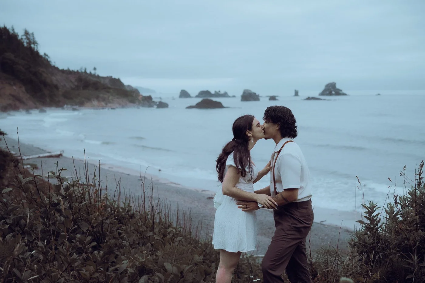 An engaged couple kisses in the moody weather of Indian Beach