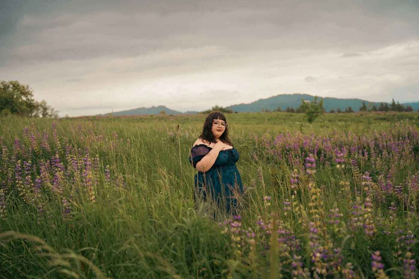 A girl in a gothic dress stands in a field of tall grass and flowers