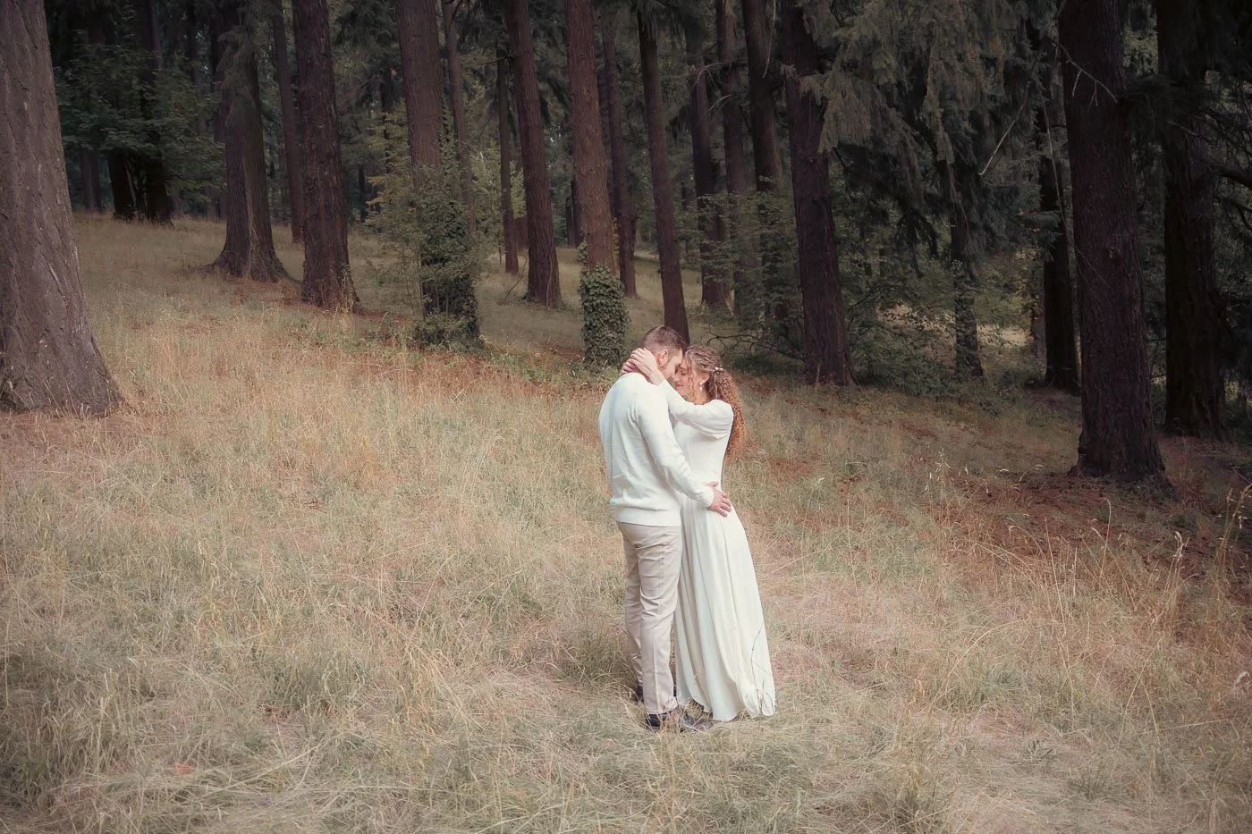 A couple in all white embraces in a forest at Mt Tabor