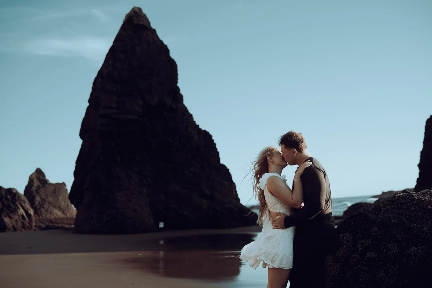 Large rock formations surround an engaged couples on the beach