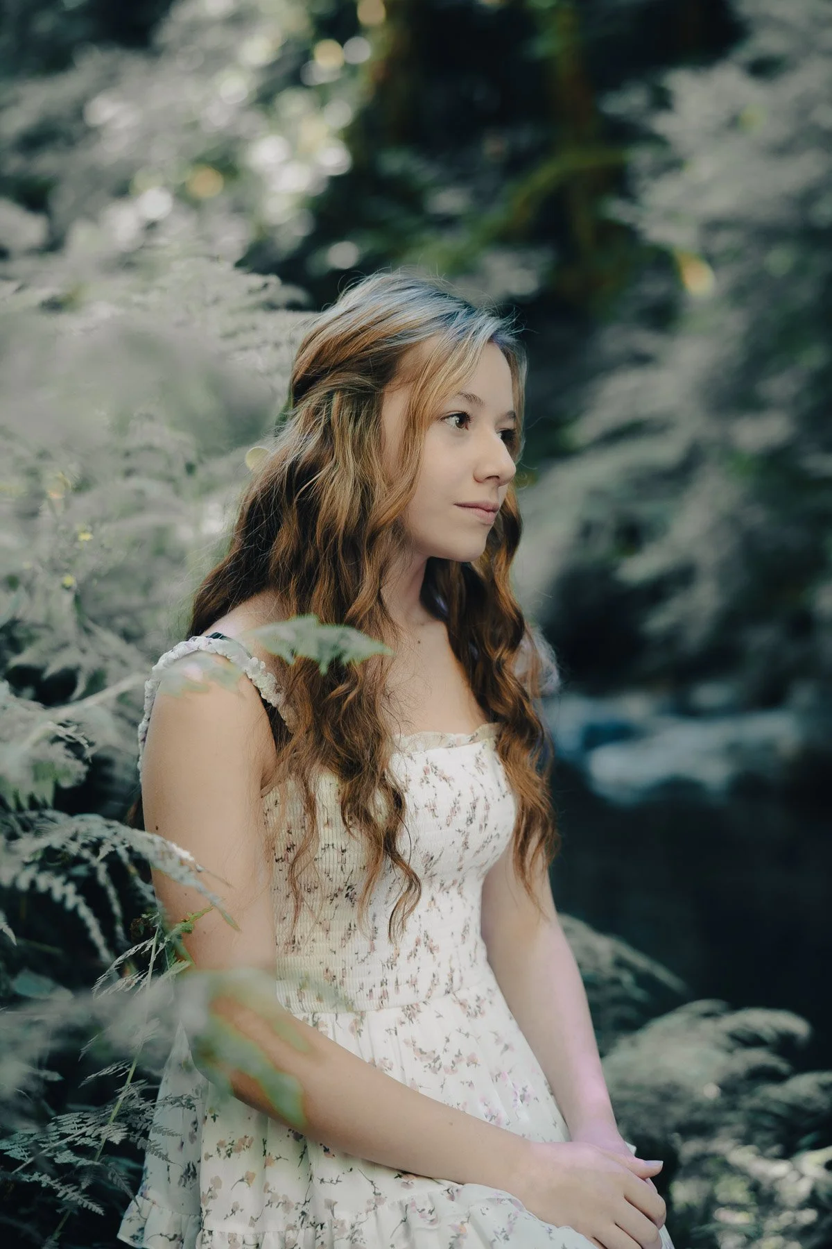 A girl in a white dress, surrounded by ferns at the edge of a river