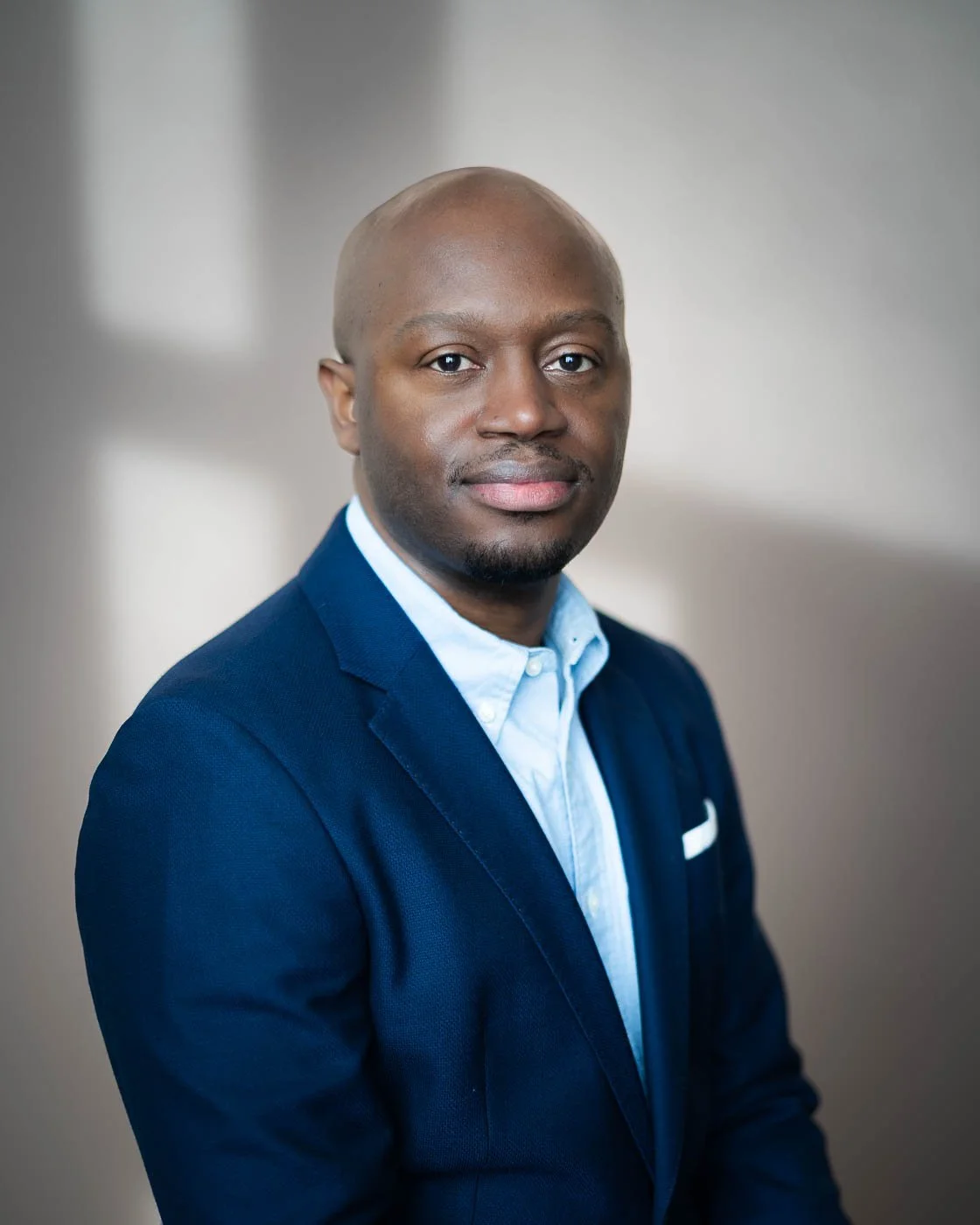 Headshot of a black man in a blue suit, set against a patterned shadow background