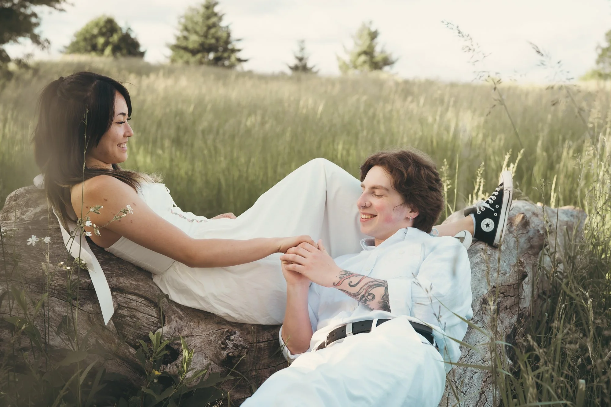 Engagement photography of a couple laying on a downed tree in a meadow of tall blonde grass