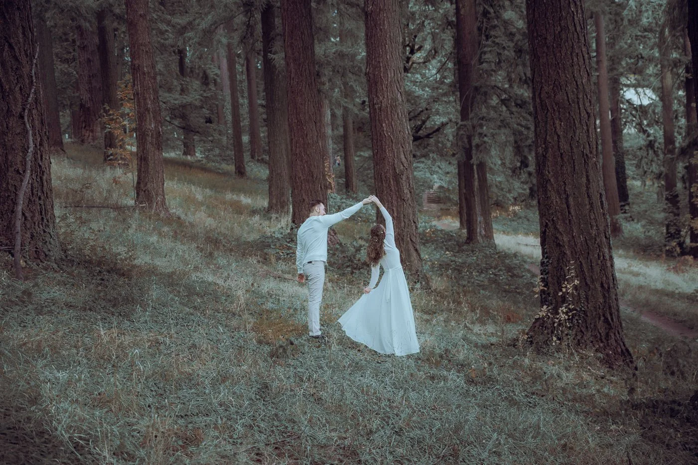 A couple in all white dancing amongst tall trees