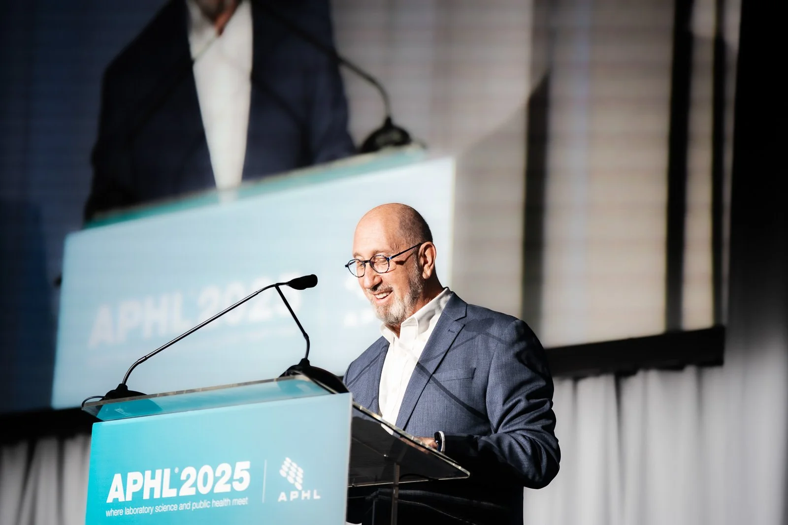 A man on stage with a Jumbotron behind him, giving a speach 