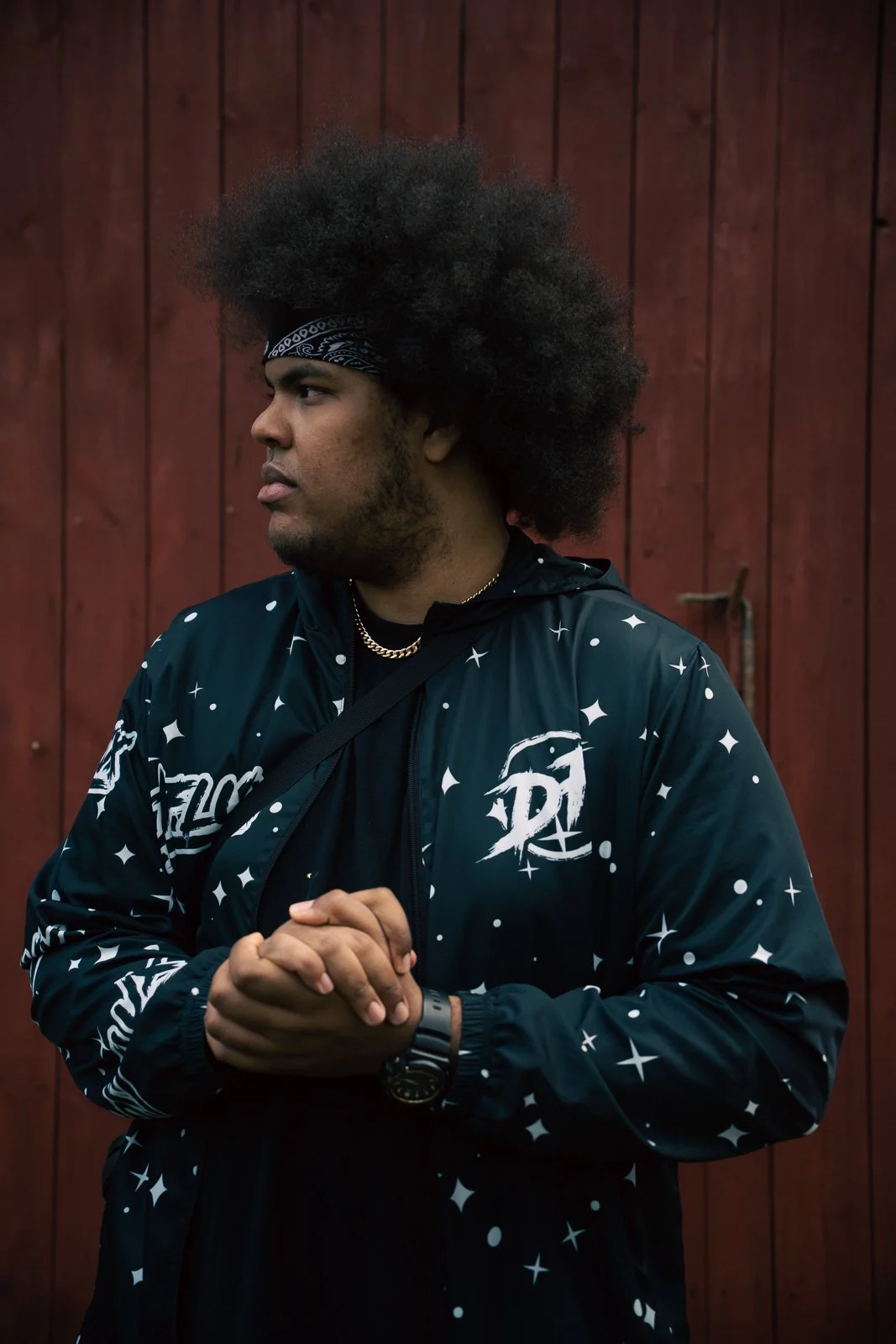 A male rapper standing looking to the side, in front of a red wall