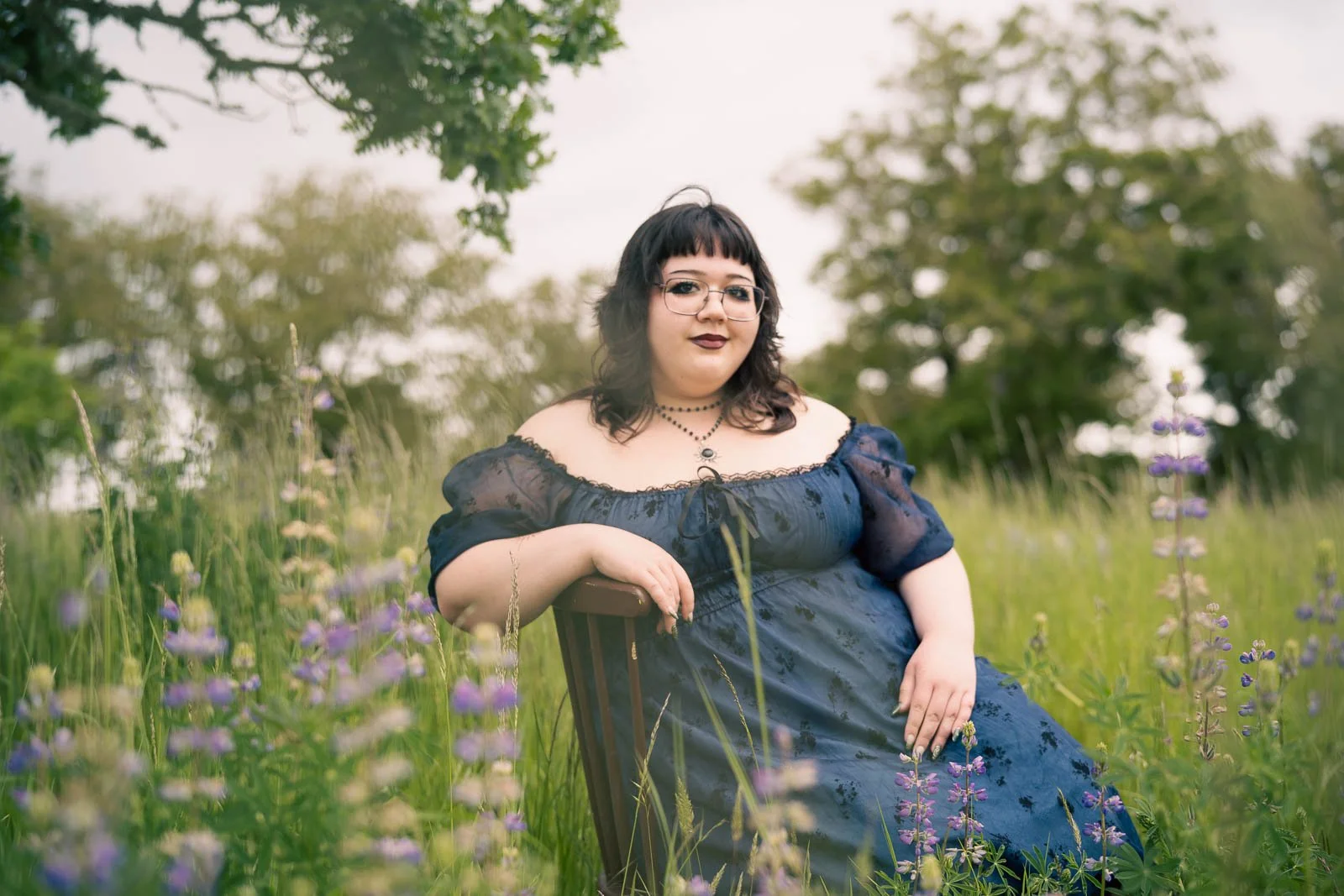 Girl in a black dress sitting in chair in a field or purple flowers
