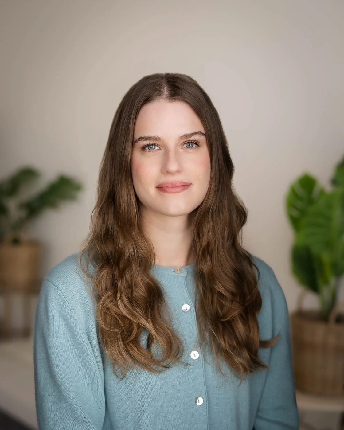 Closed mouth smile headshot of a woman in a pastel blue shirt with long curly hair