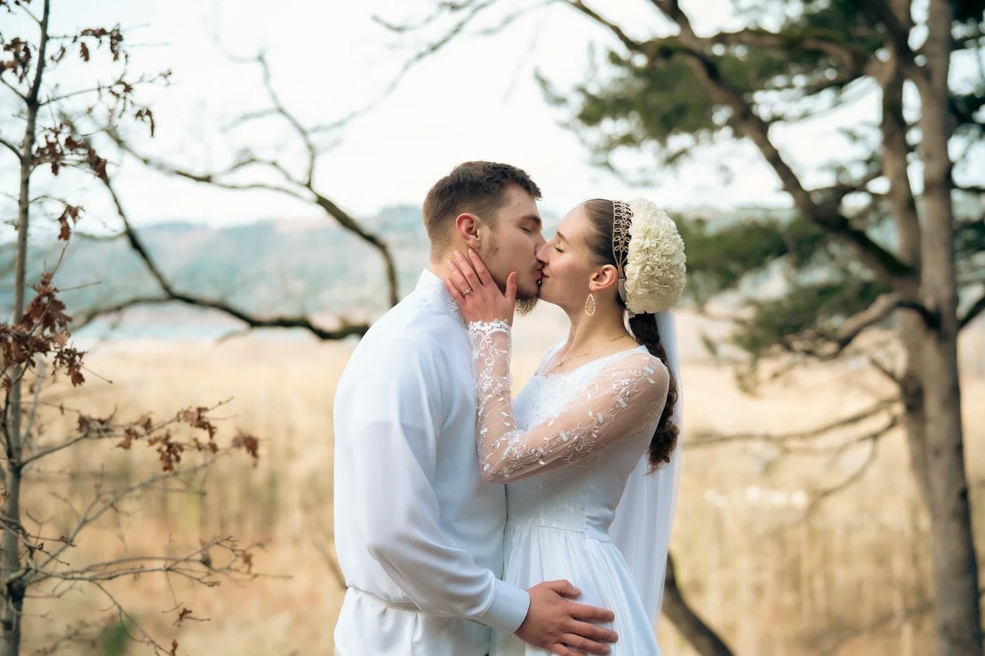 A couple dressed in all white kisses in front of golden trees near Multnomah Falls