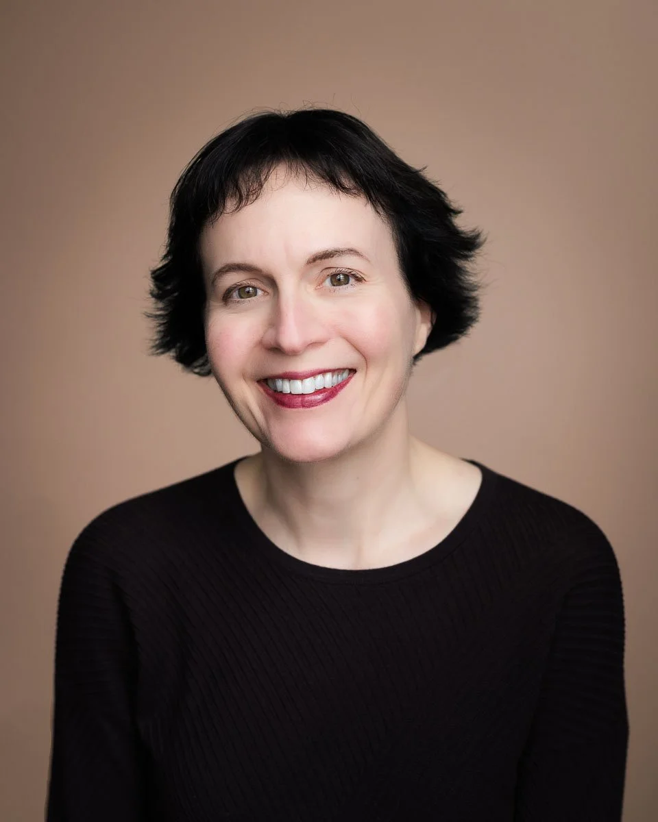 A smiling woman with short black hair posing for a headshot against a neutral colored background.