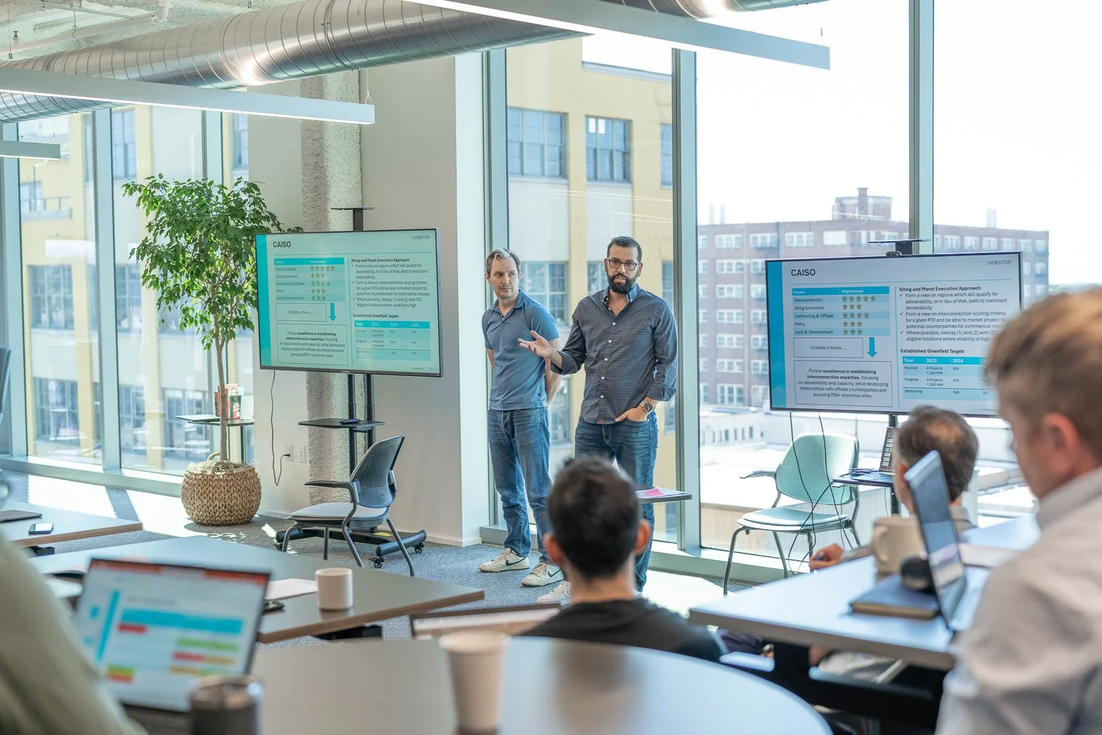 Two presenters at a Gridstor employee work meeting in a room with large windows