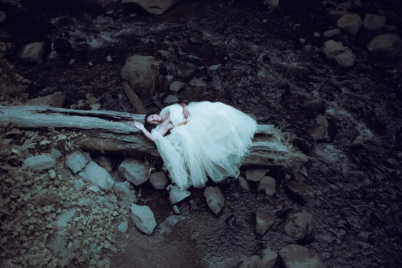 A girl in a white dress dramatically laying on a log in the river at Latourell Falls