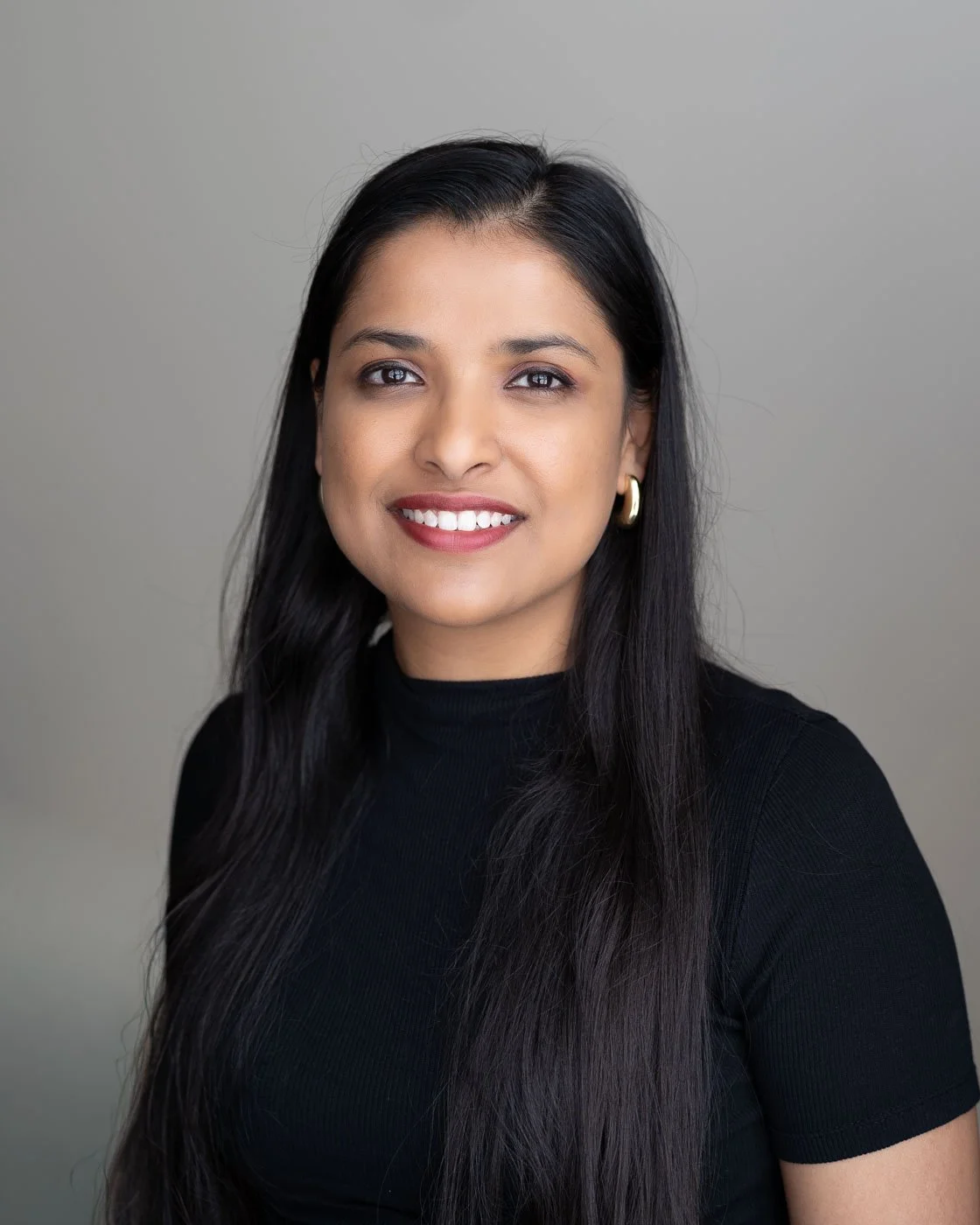 Headshot of an Indian woman with a friendly smile against a light grey background