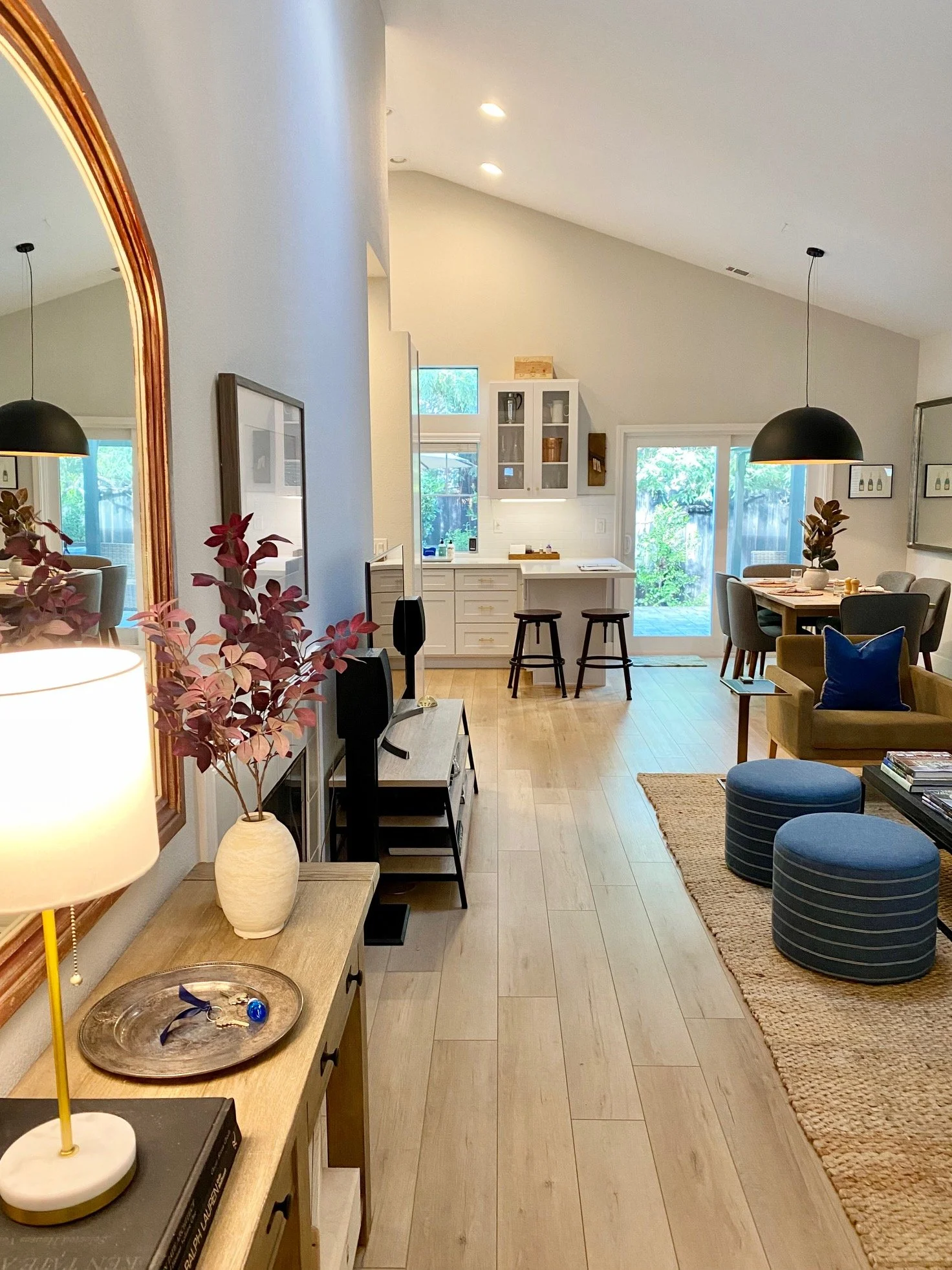 View of a bright open-concept living space with a kitchen, dining area, and living room, featuring wooden floors, modern furniture, and sliding glass doors leading outdoors.