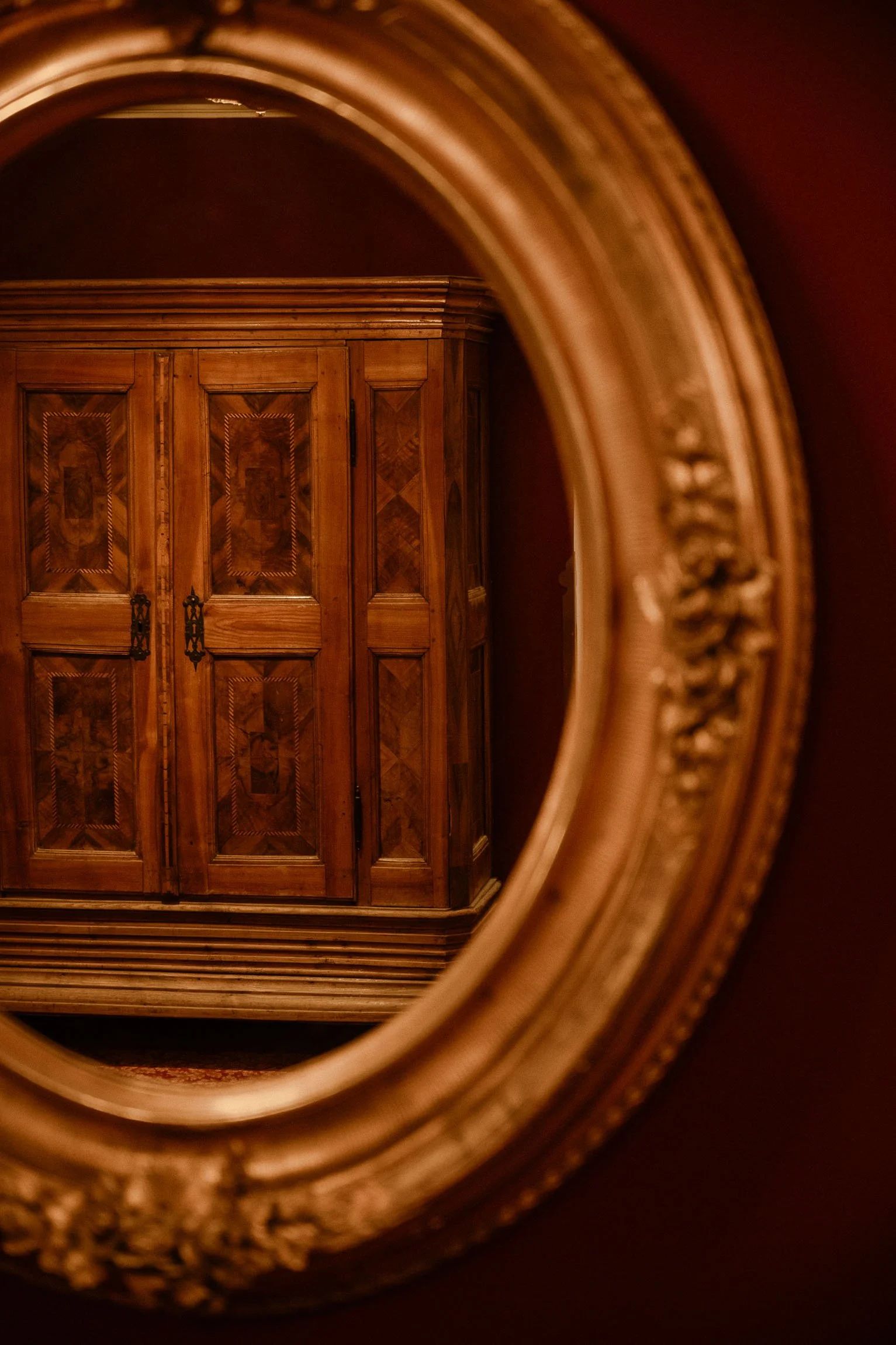 Ein eleganter, in einem Spiegel reflektierter, antiker Holzschrank mit aufwendigen Verzierungen und dunklen Beschlägen, vor einem dunklen Hintergrund.