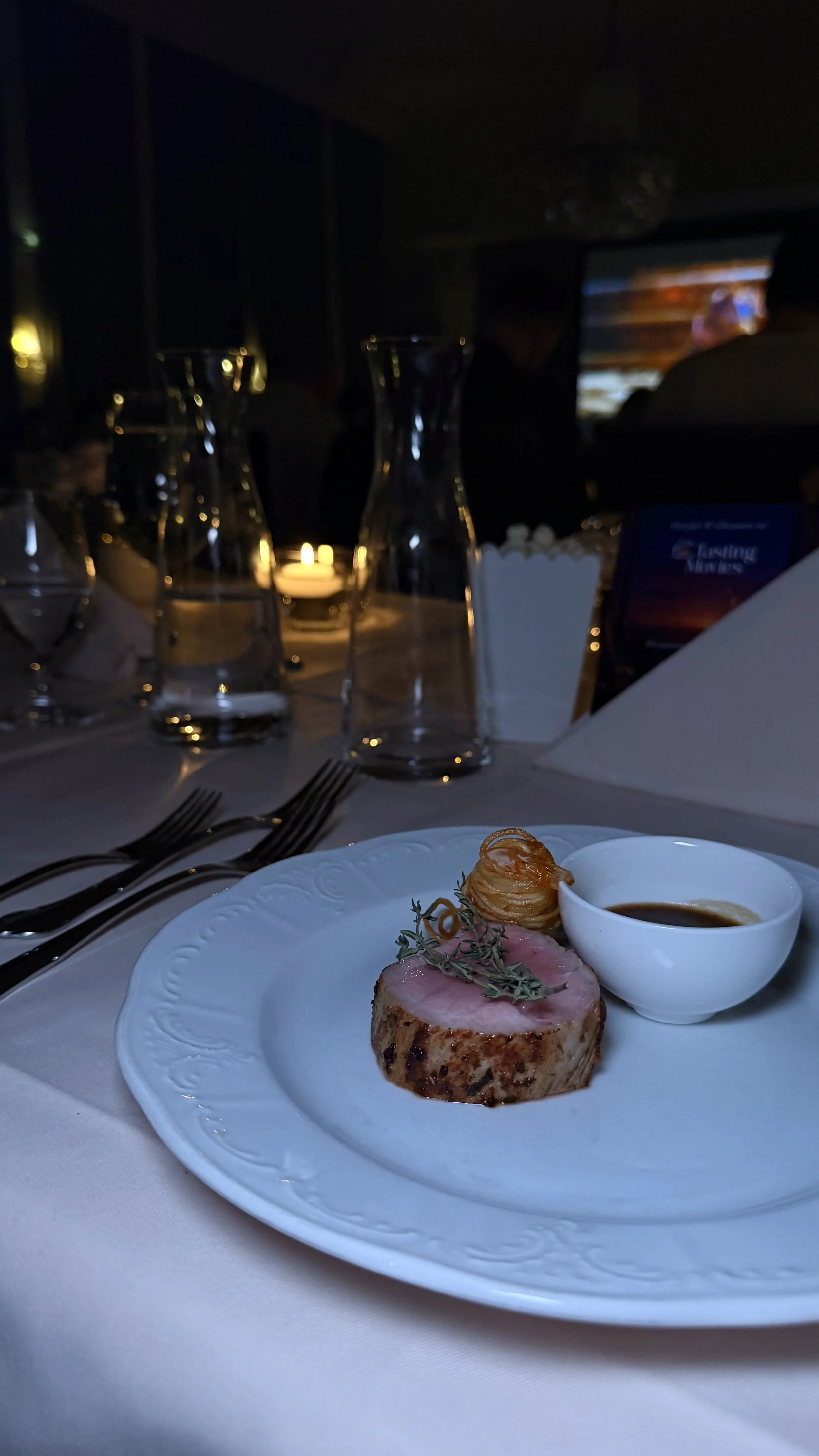 Ein Teller mit einem saftigen Steak, einer kleinen Schale mit Sauce und einer kleinen Kartoffelspirale, serviert in einem eleganten Restaurant.