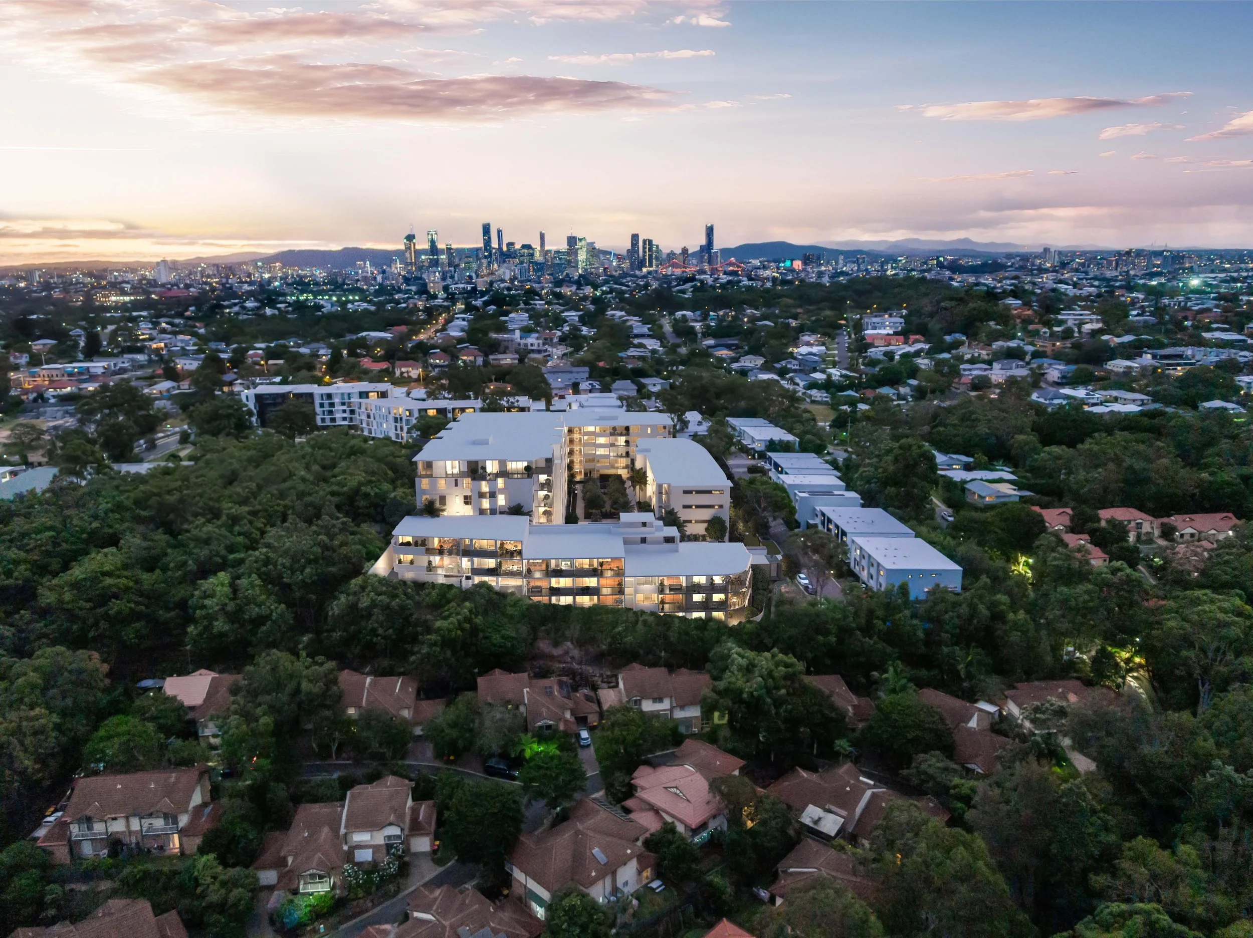 Aerial view of a city skyline during sunset with a mix of residential houses and tall downtown buildings, and a hilly background.