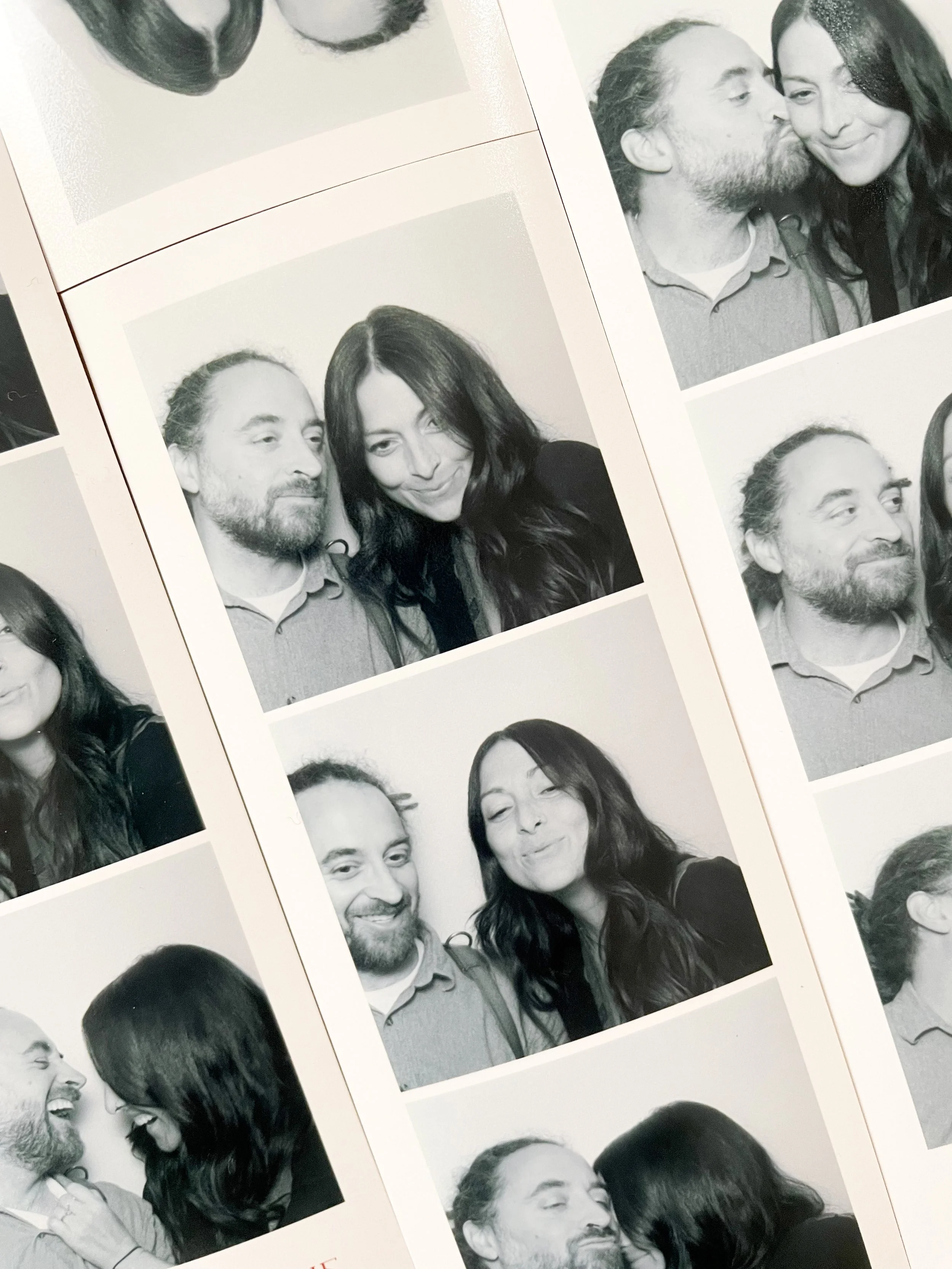 Photo booth strip with black and white pictures of a couple making various facial expressions and gestures, including smiling, winking, and leaning towards each other.