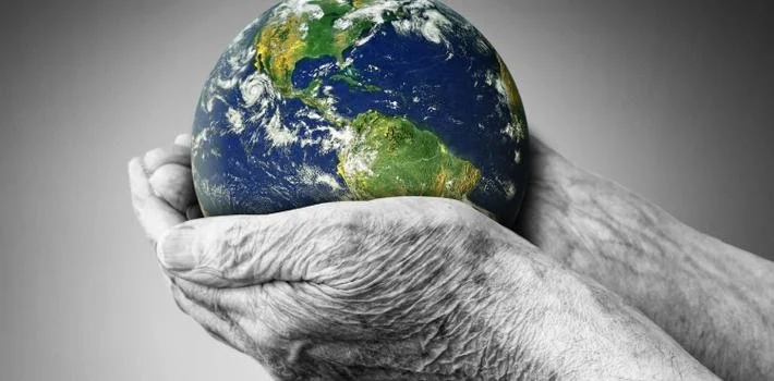 Old hands holding a small Earth globe, symbolizing care for the planet.