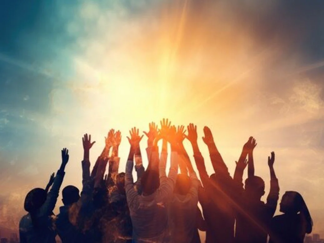 Group of people with hands raised towards the sky during sunset or sunrise, with sunlight streaming behind them.