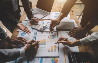 People analyzing charts and graphs on a table with laptops and notebooks.