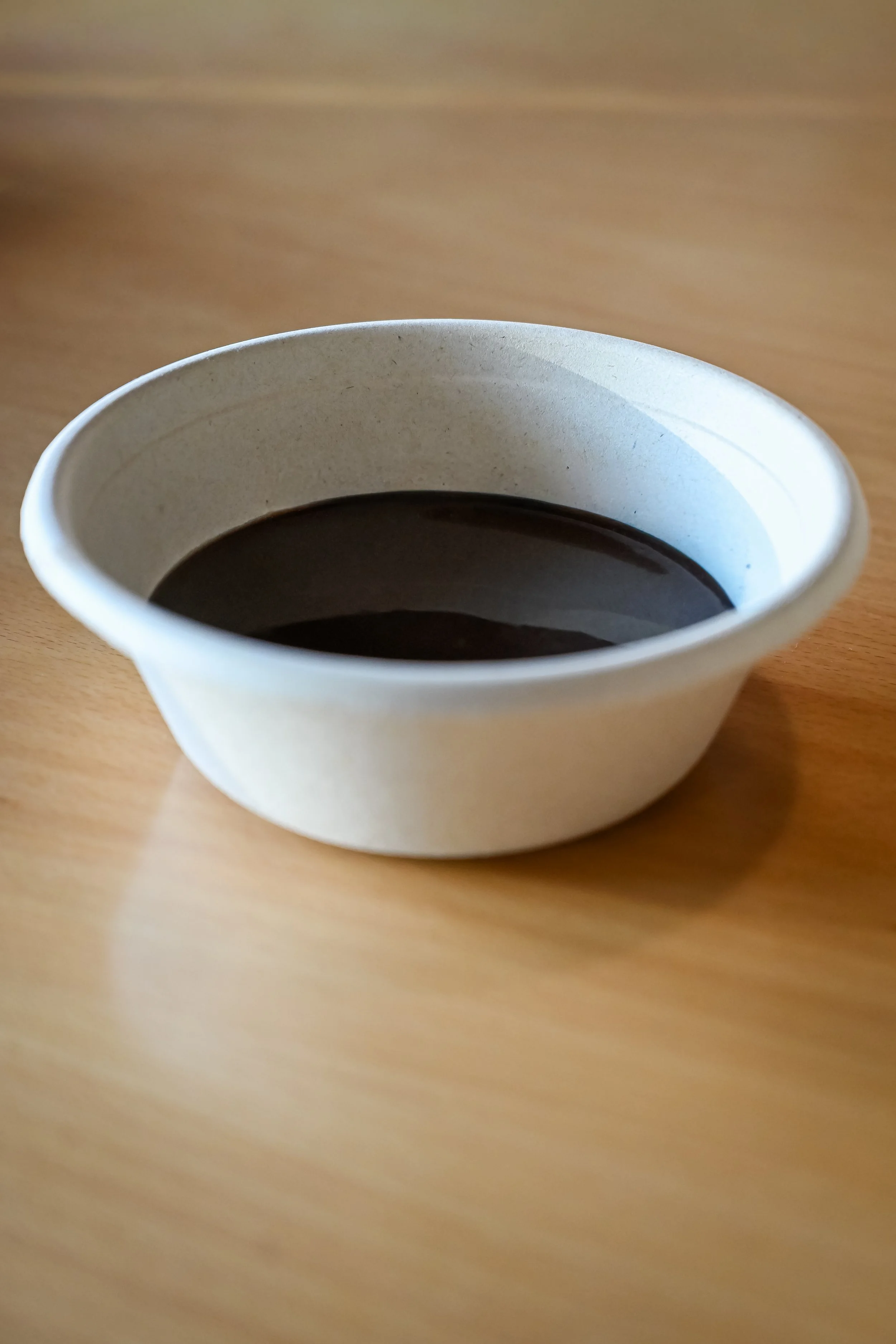 A paper cup filled with black coffee on a wooden surface.