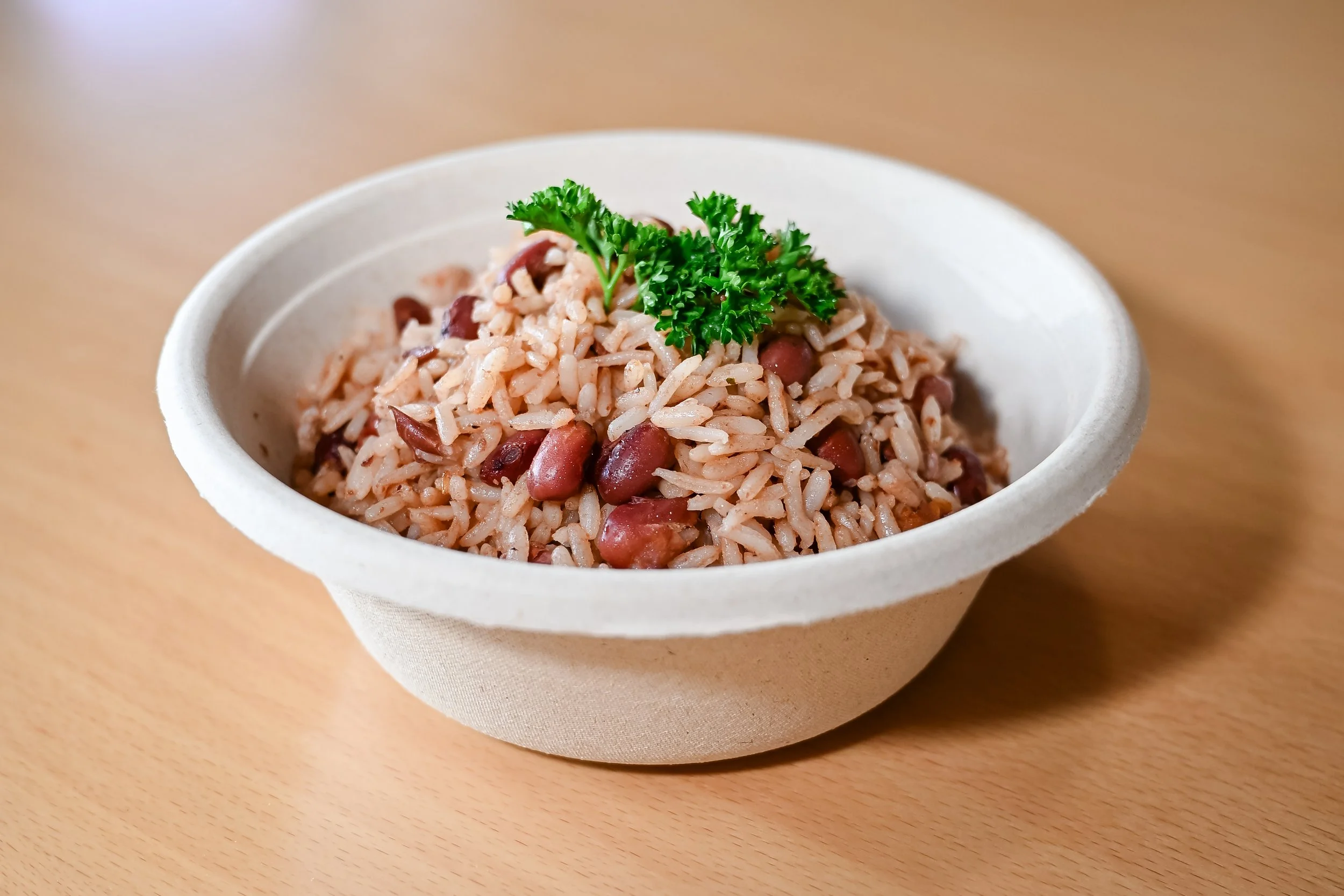 A bowl of rice and beans garnished with a sprig of parsley on a wooden table.
