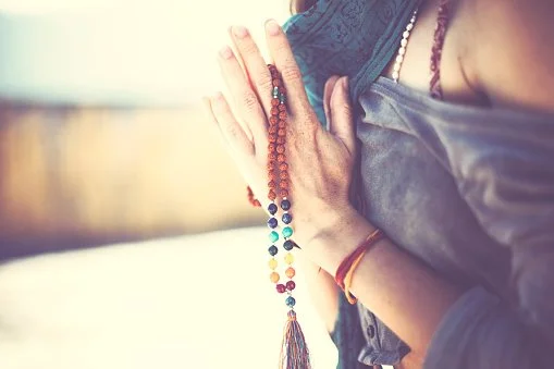 Person holding prayer beads with hands pressed together in a prayer or meditative pose.